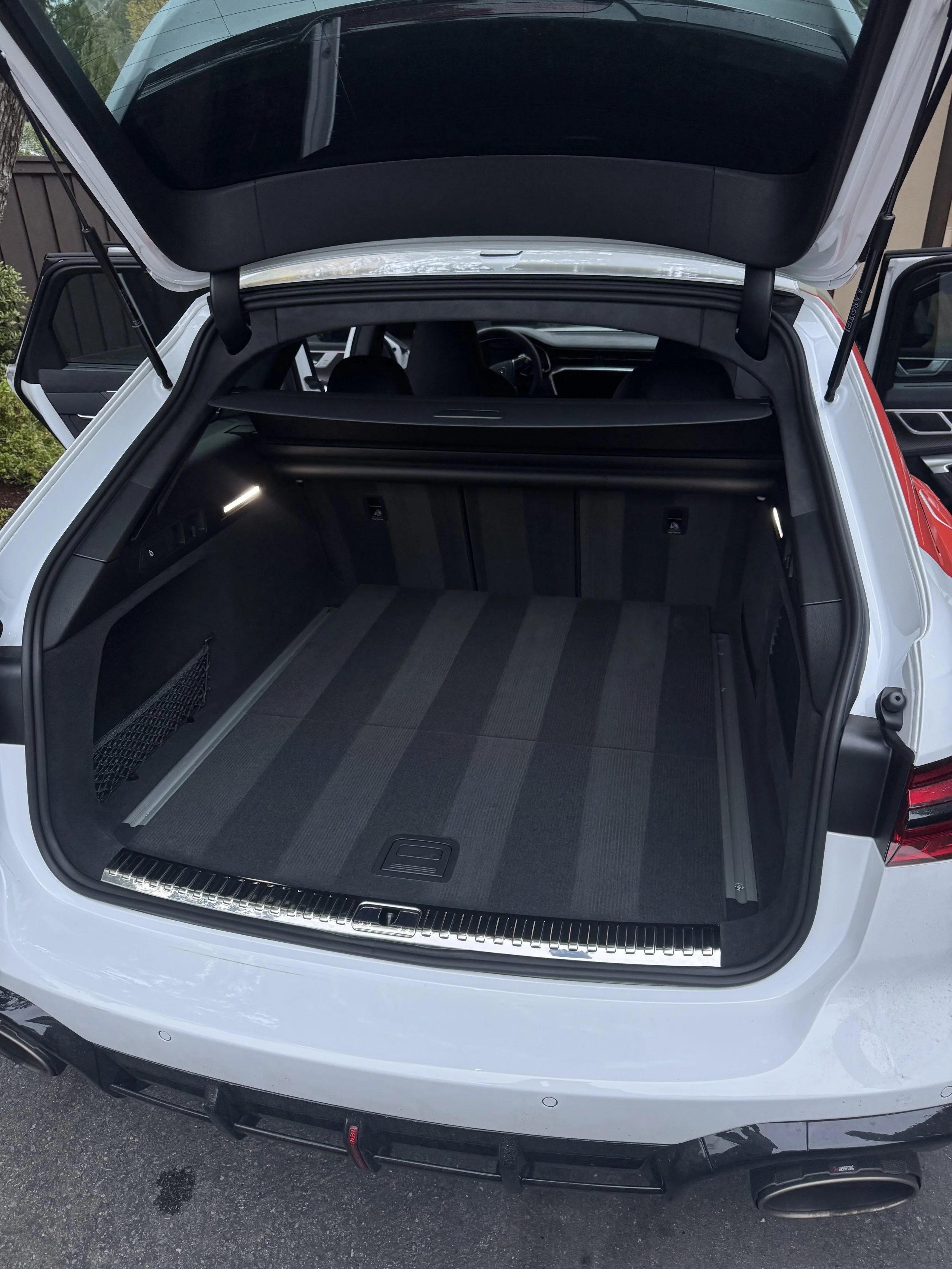 Open trunk of a white sports utility vehicle showing a spacious cargo area with a retractable cover, black interior, and rear seats.