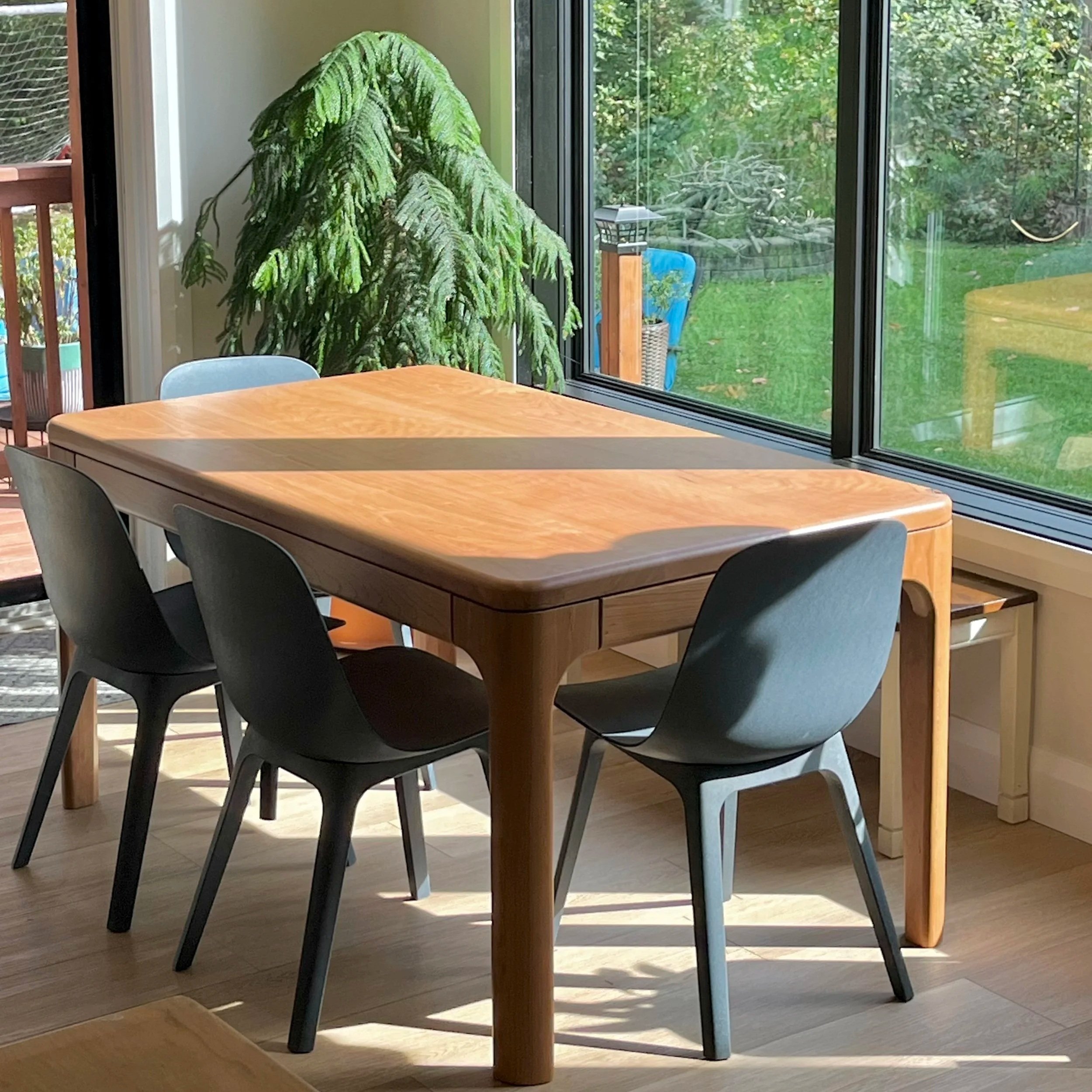 corner view of a rounded cherry dining table with 5 black chairs placed around it