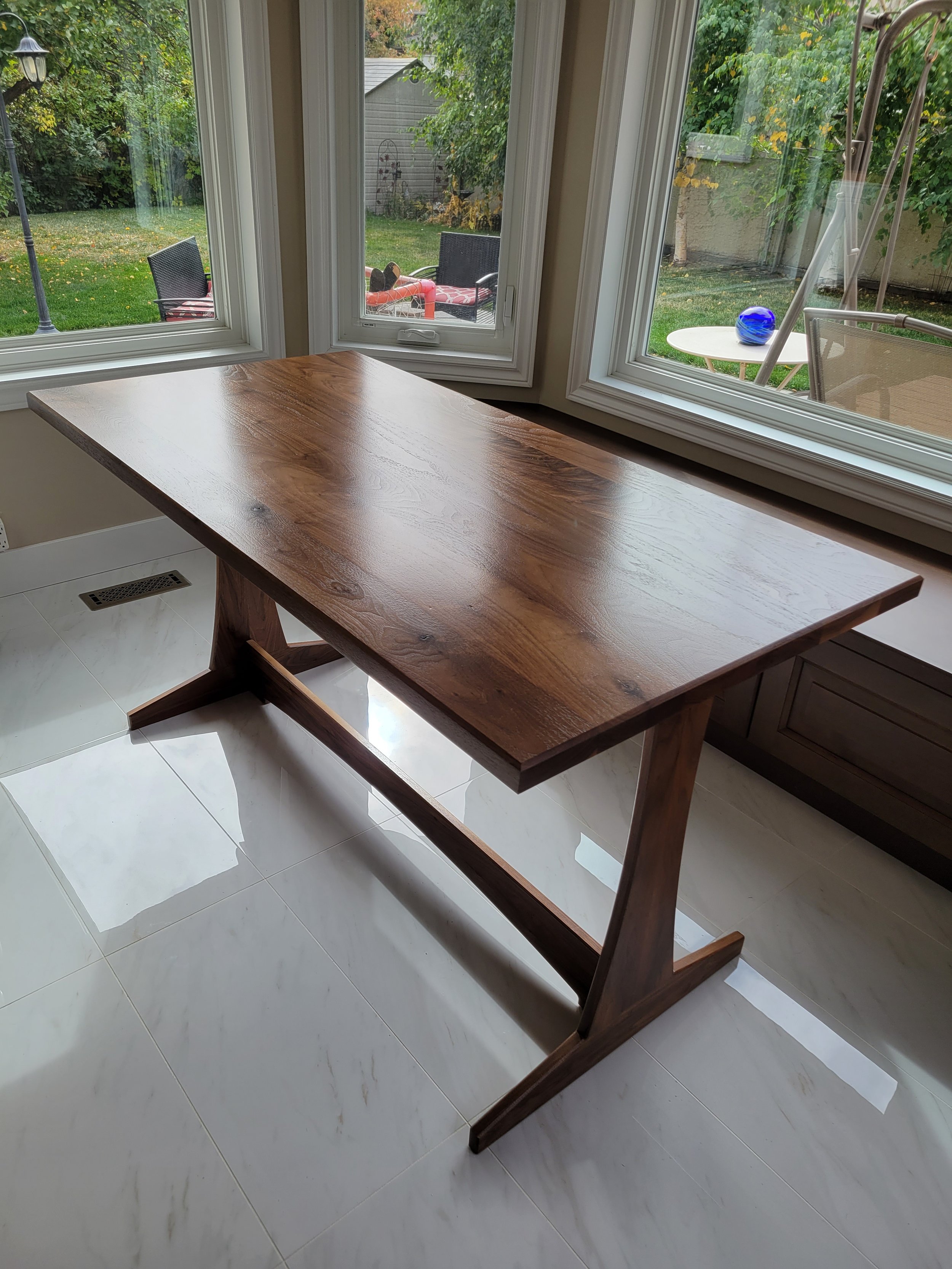 View from the corner of a walnut trestle table tucked into a small breakfast nook