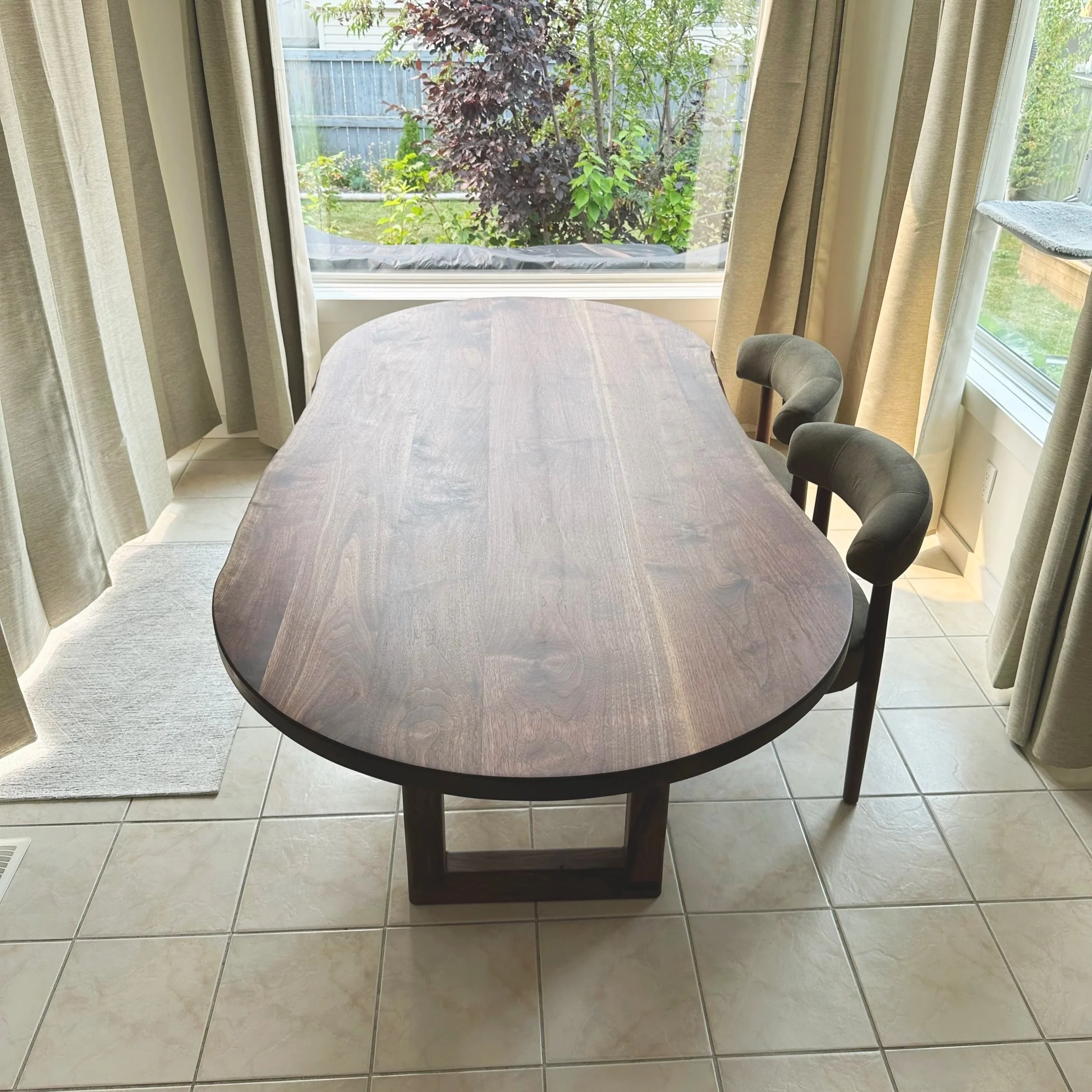 End view of a live edge walnut dining table with rounded ends and green chairs
