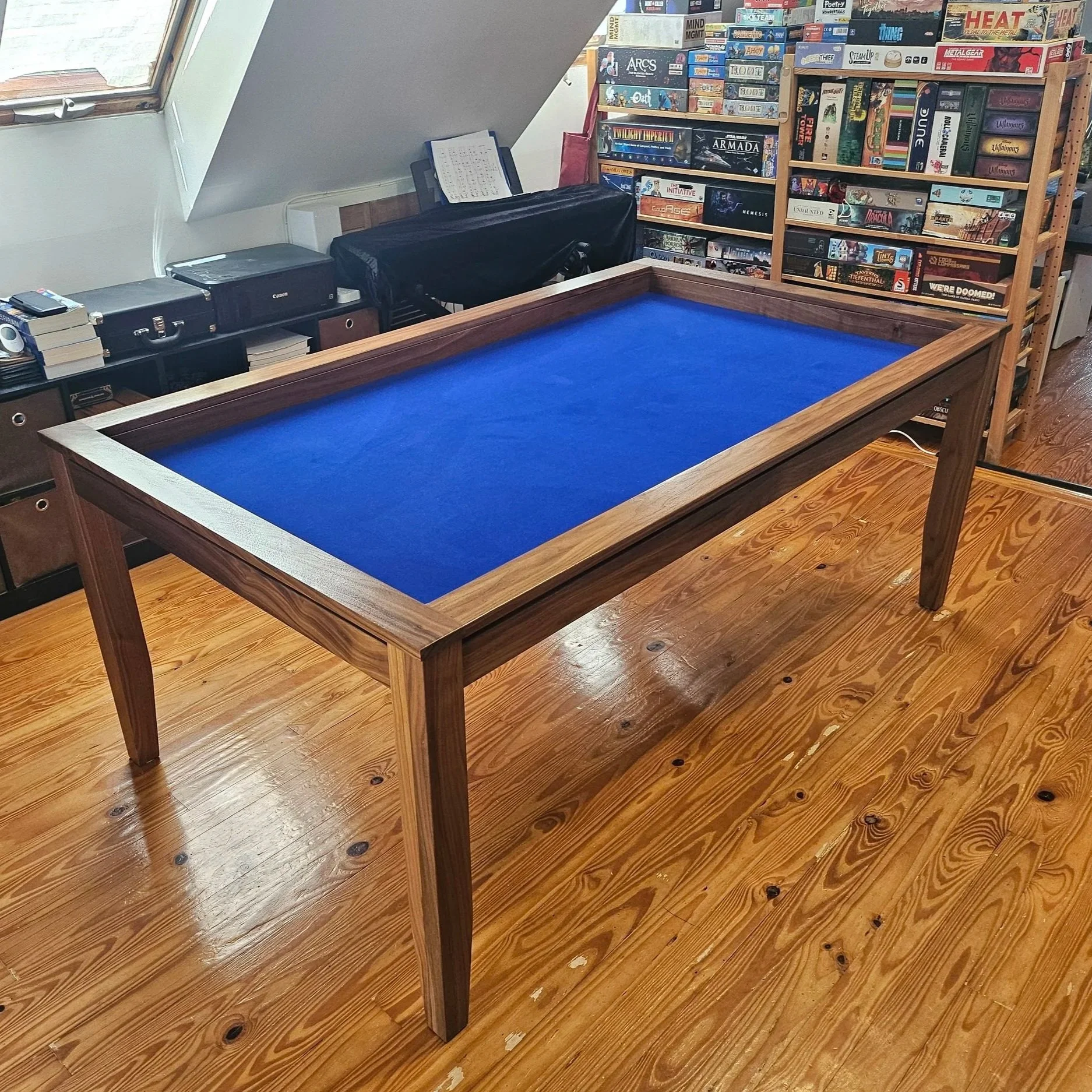 View from the corner of a game table showcasing the entire table in front of a bookshelf full of board games