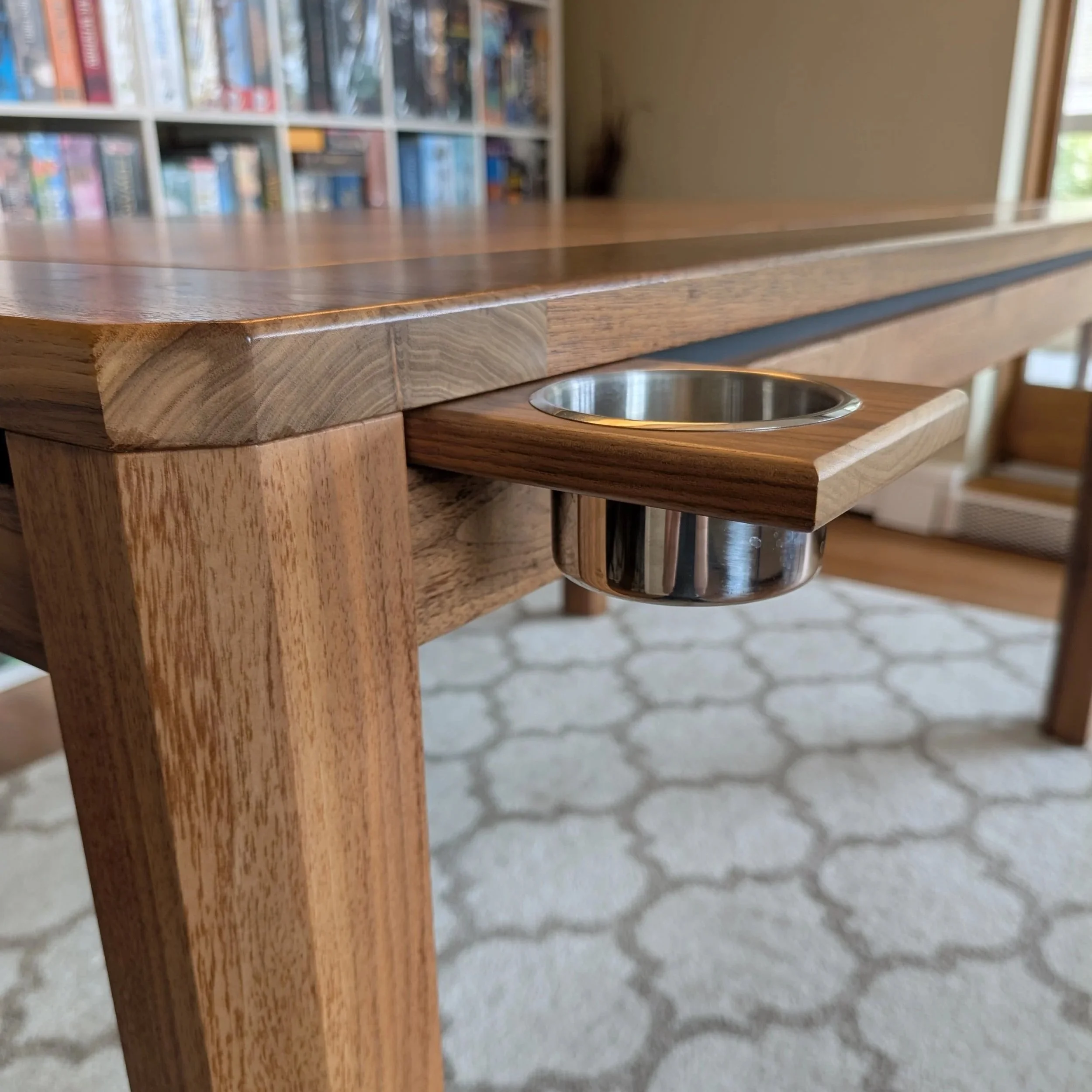 Close-up of a stainless steel cupholder built into the side rail of a walnut board game table.