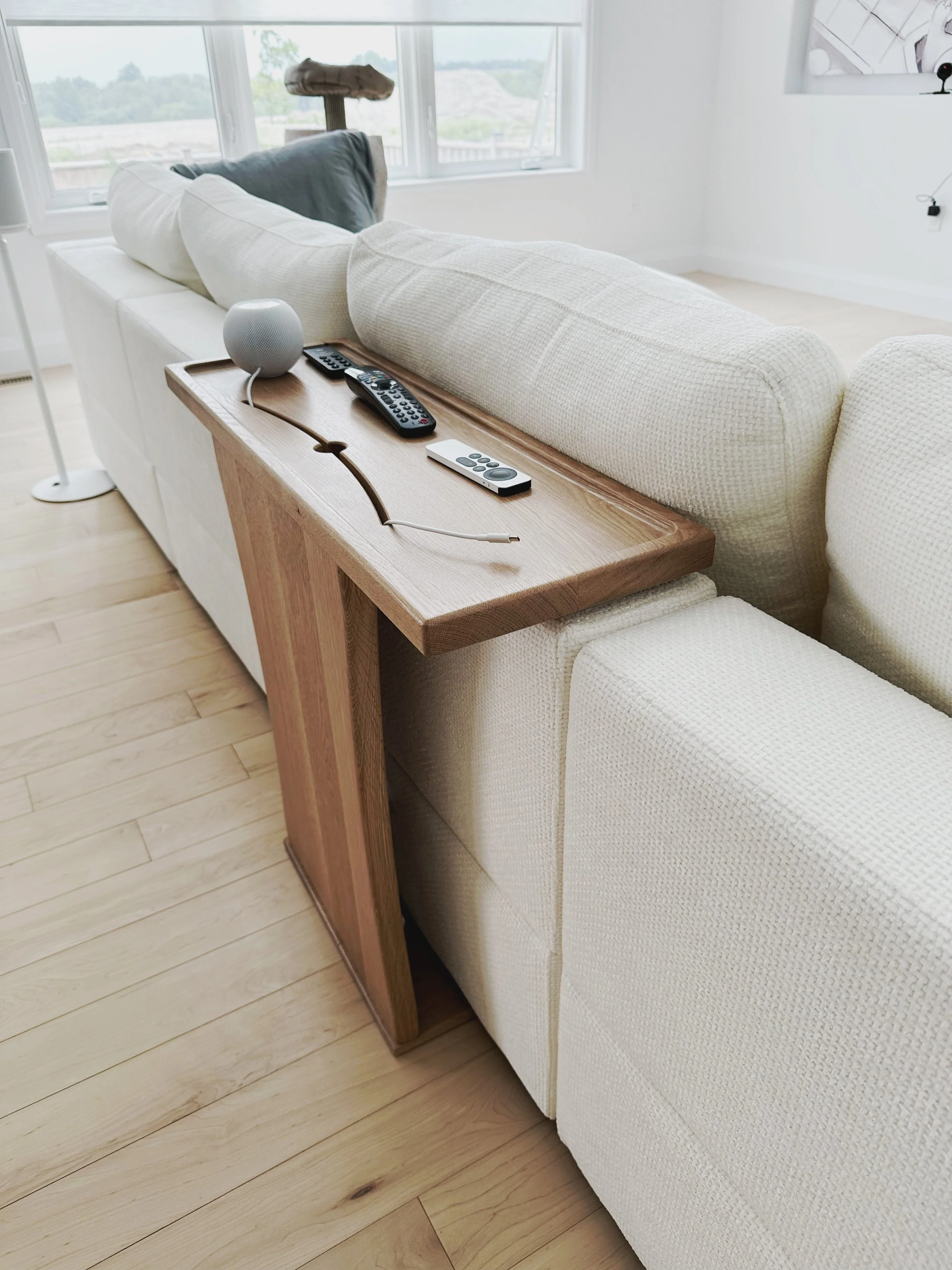 Corner view of a white oak couch table wrapped up the back of a couch with recessed top that has holes for cords to pass through