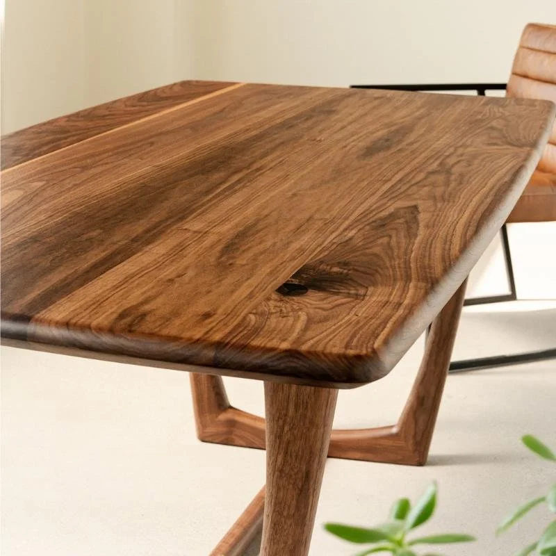 close up view of the corner of a walnut dining table with rounded corners a beveled bottom and a sleek trestle base
