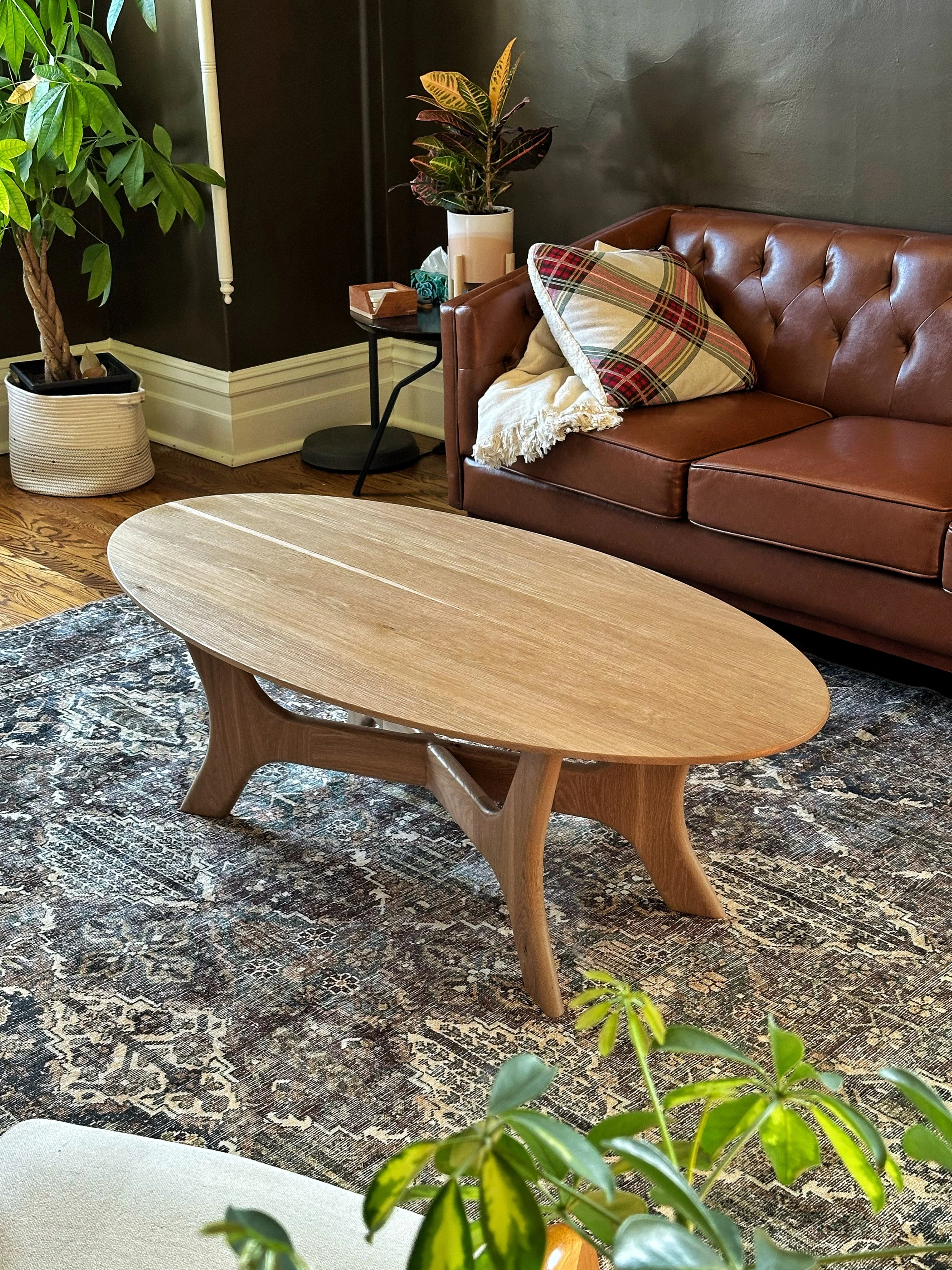Full view of a modern oval white oak coffee table with modern crossed base