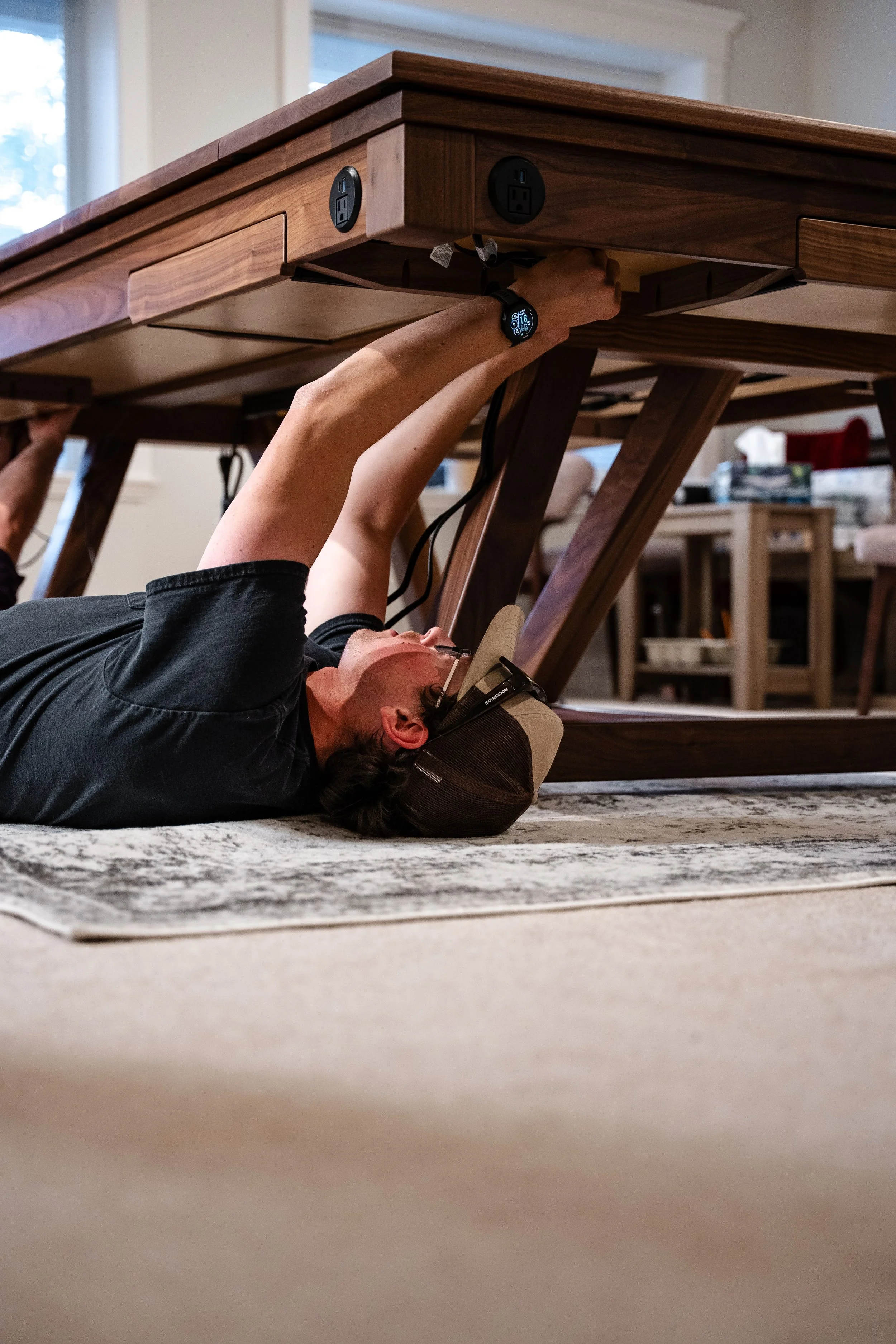 Harley Griffin laying on the floor installing cable management on a custom game table