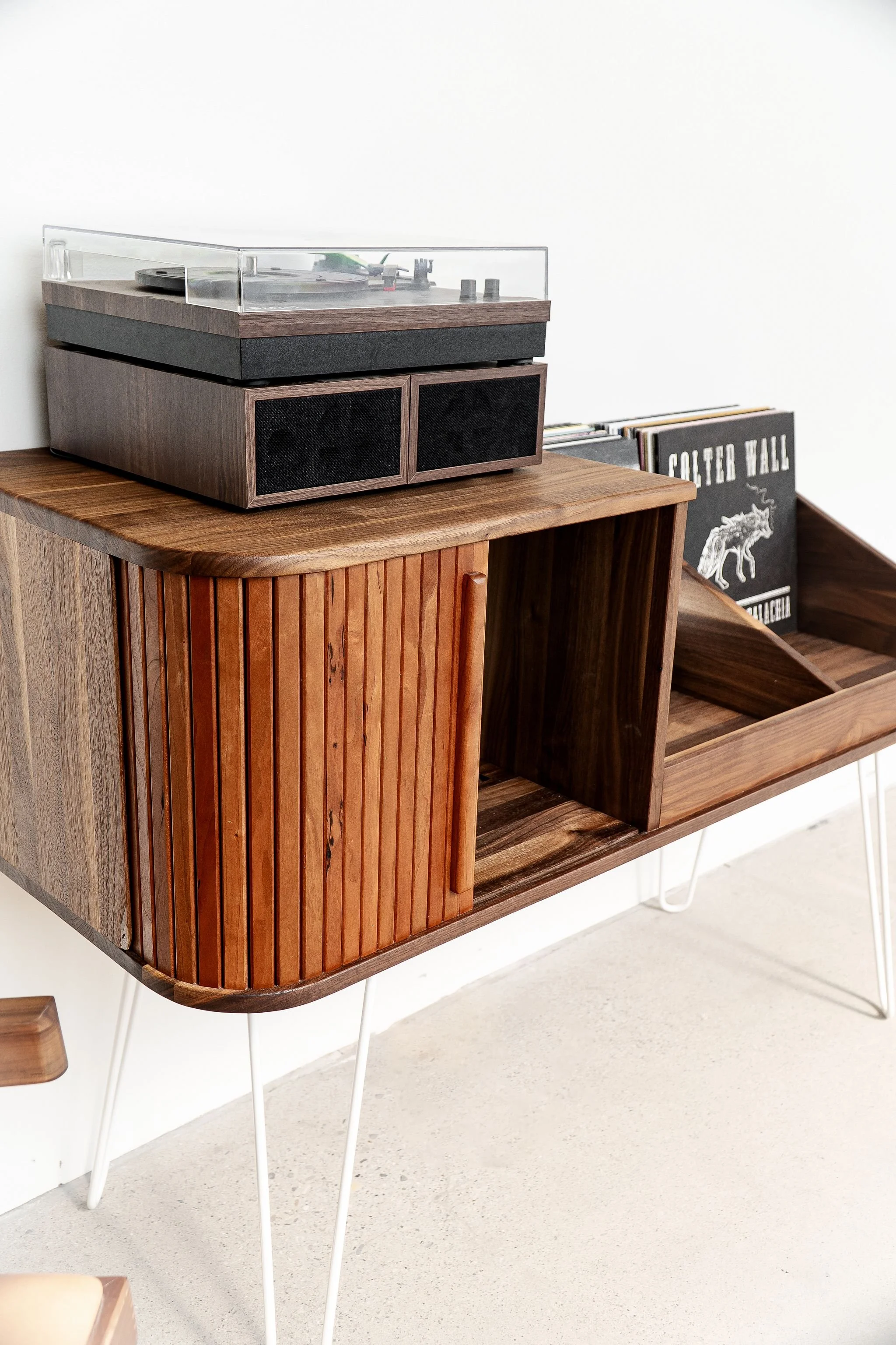 Close up view of a record cabinet that has a lareg storage area with cherry tambour door and 2 large open bins for more record storage and a space on top for a record player to sit