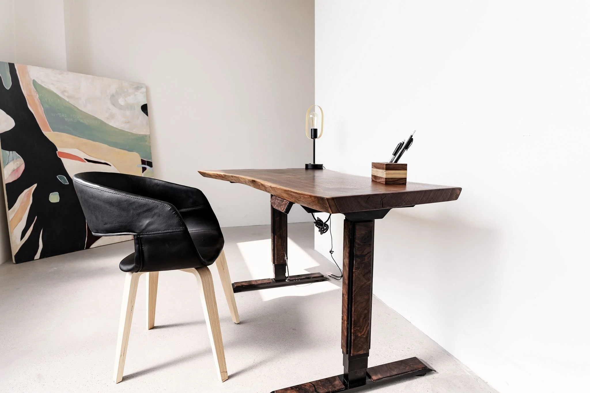 A walnut live edge slab atop a standing desk table lift with custom wooden accent fixed to the base