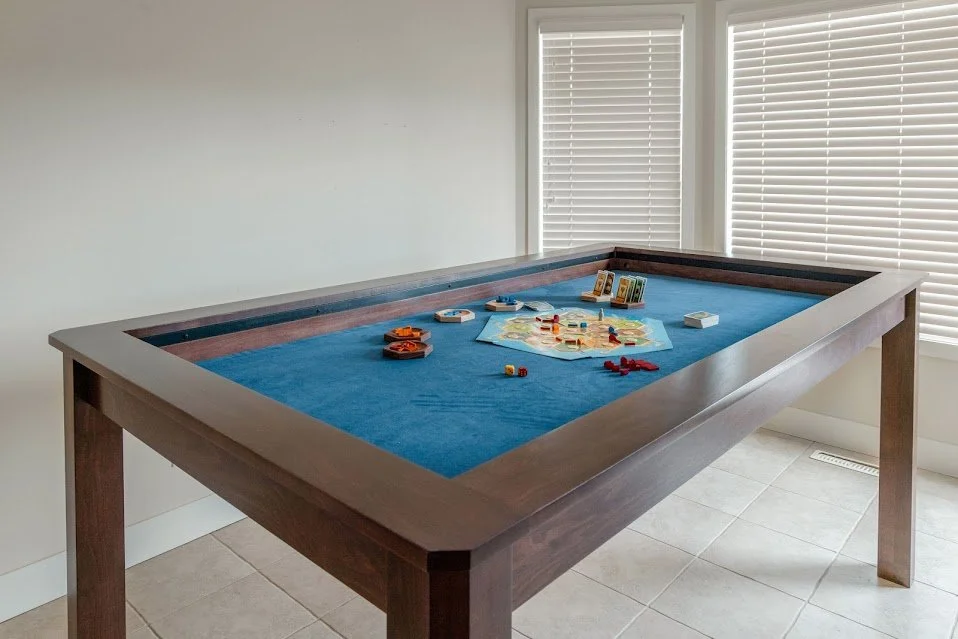 Low corner view of a stained sleek game table with a board game setup on a blue neoprene rolling mat.
