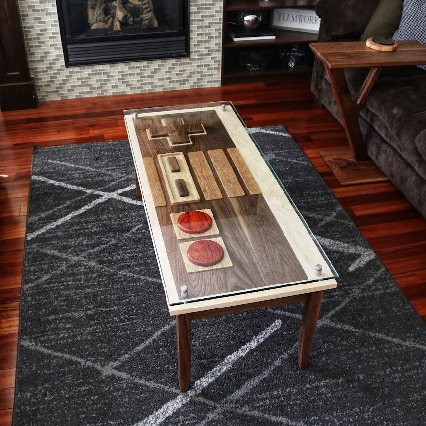 A Nintendo inspired controller coffee table using natural colored woods to achieve the different buttons and accent pieces covered with a thick piece of glass