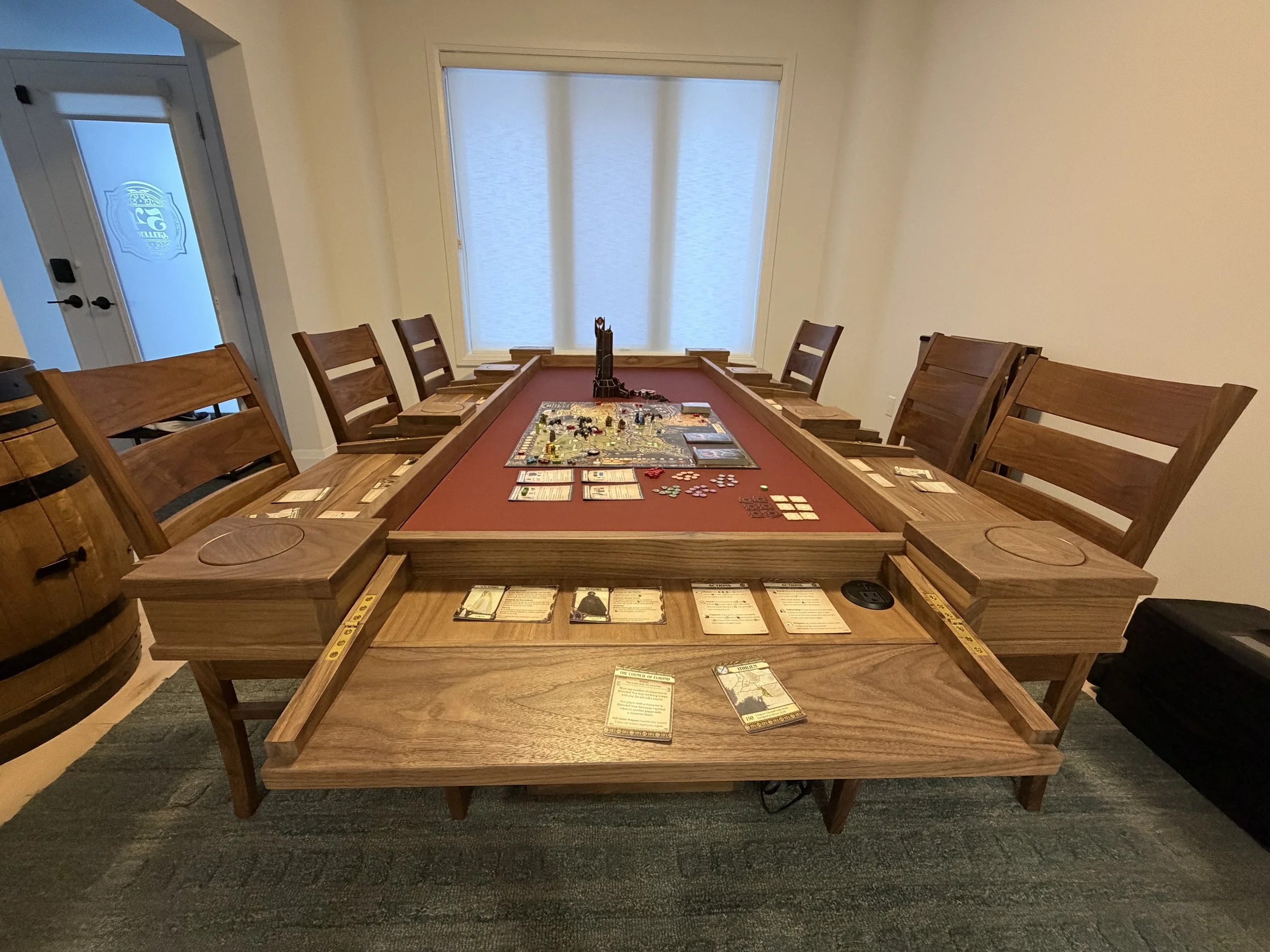 End view of a walnut player station game table with flipped out player stations a game setup in the middle of the dropped gaming area and chair set around at each station