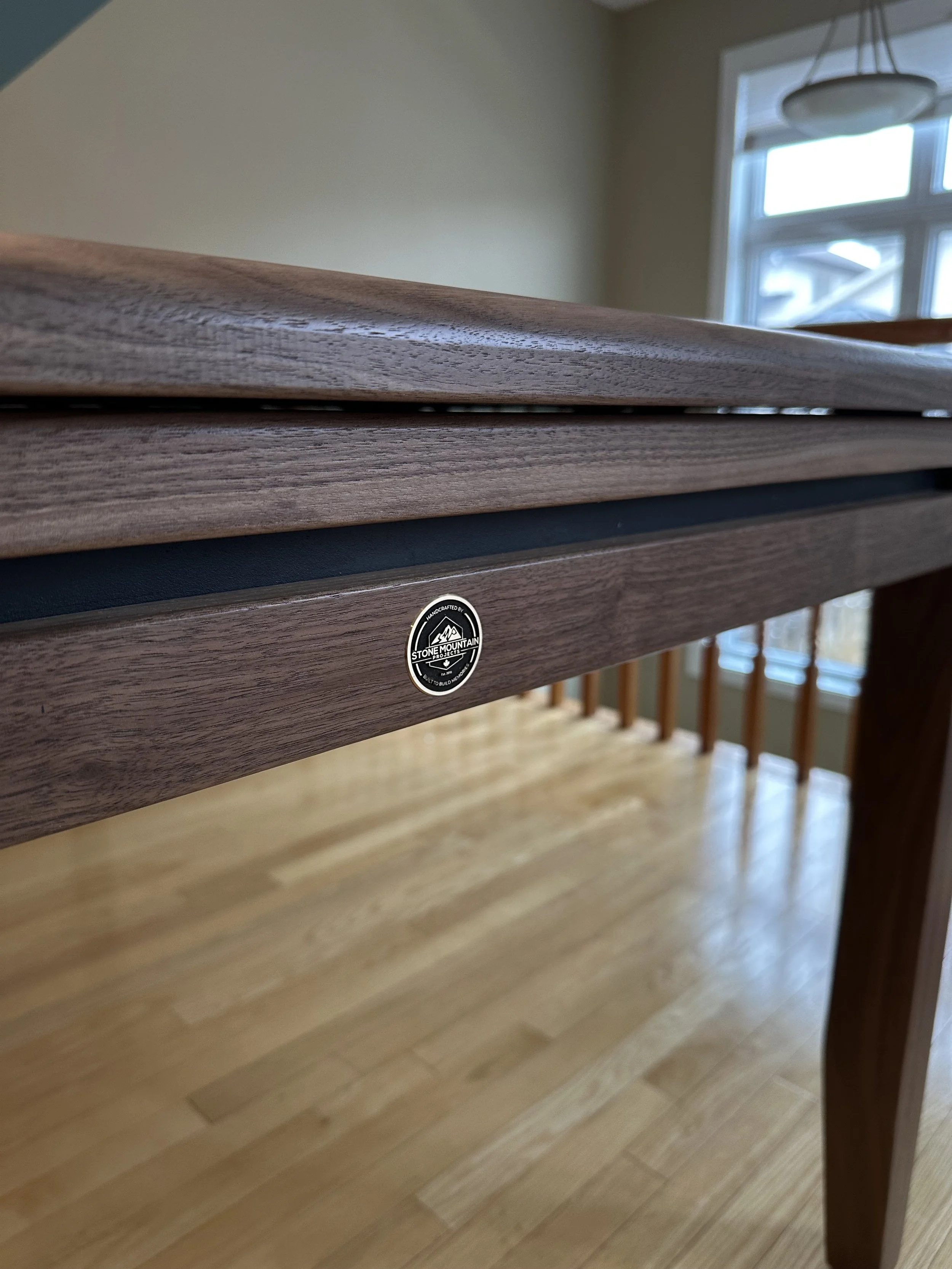 A detailed shot of the Stone Mountain Projects brass medallion that's inlaid into the end rail of the custom walnut game table