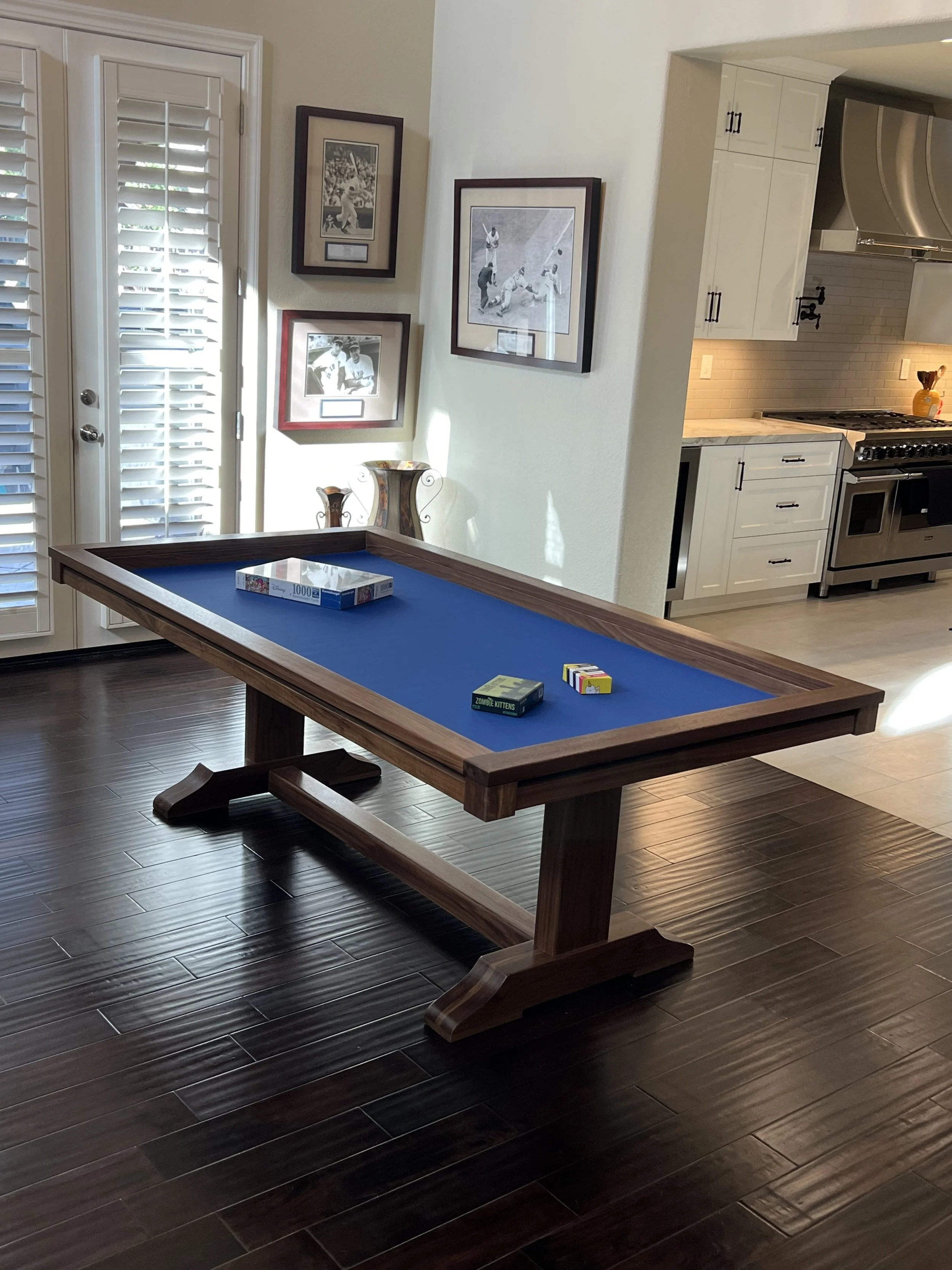 Sleek walnut board game table with a trestle base, a blue rolling mat is in the center of the table with a board game setup to play