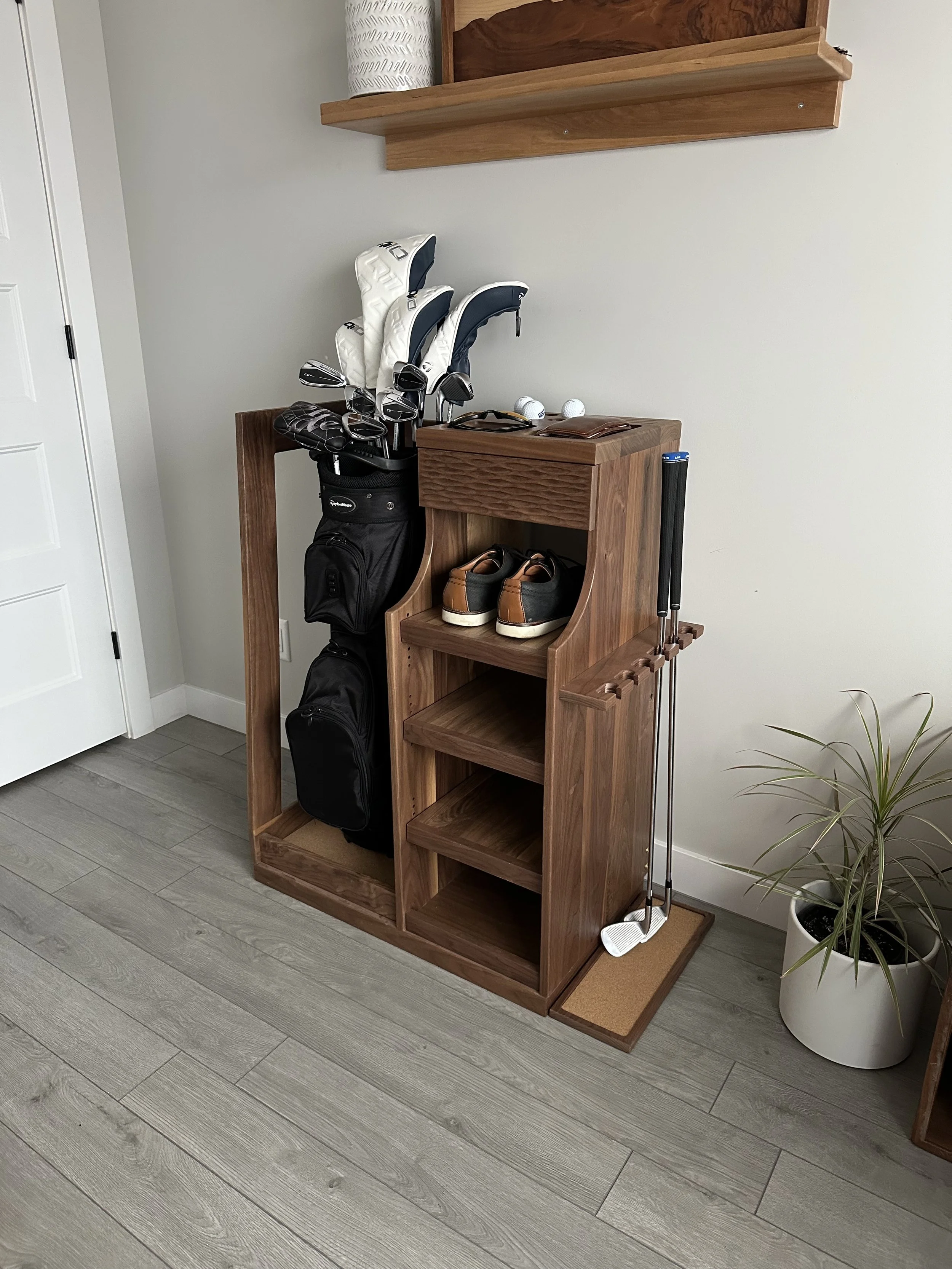 A walnut golf bag storage rack with a golf bag stored on the left and a bank of shelves and drawers on the right with golf shoes and accessories stored on them