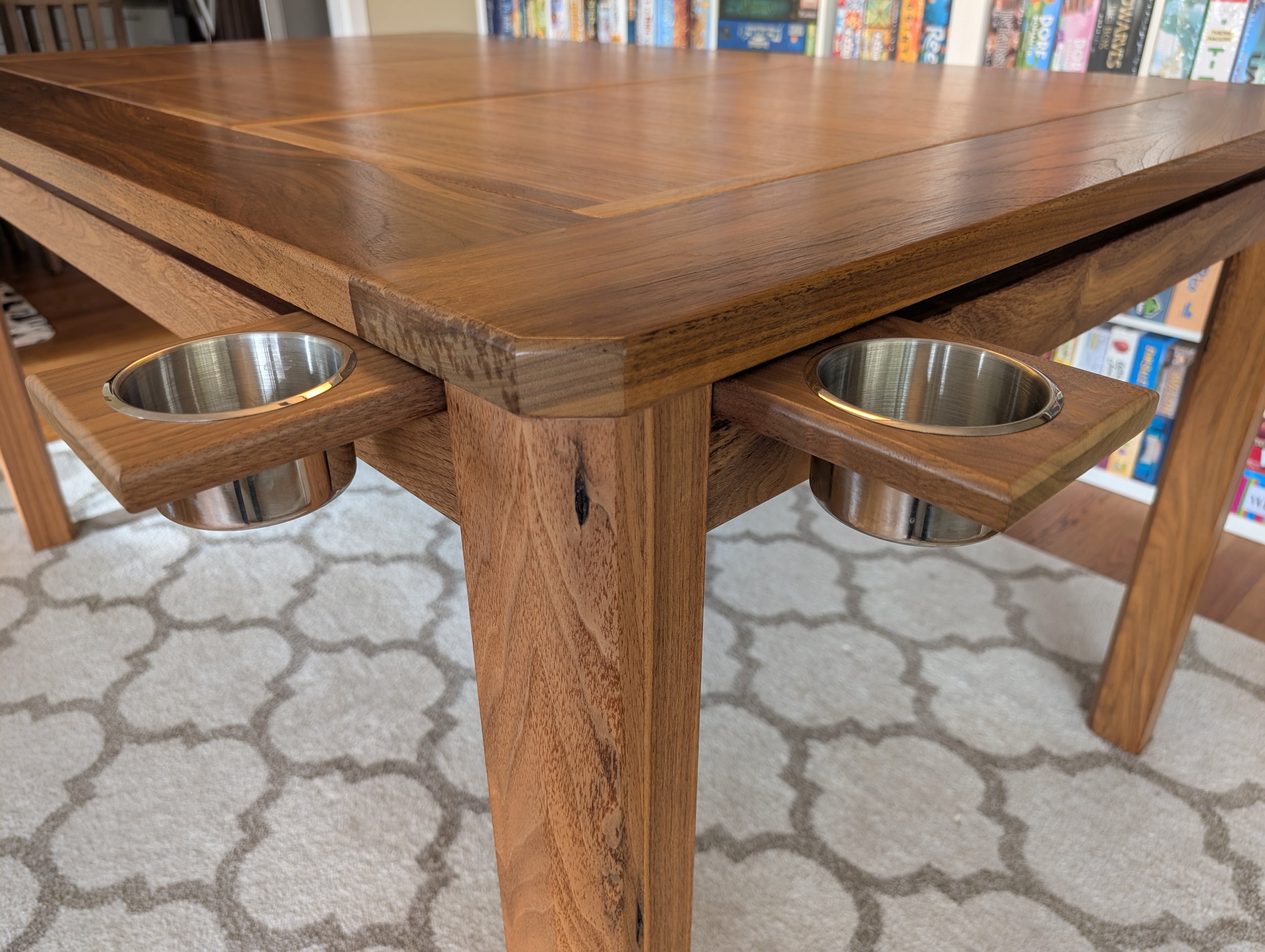 Corner detail of a walnut board game table showing two magnetic cupholders extended on adjacent sides.