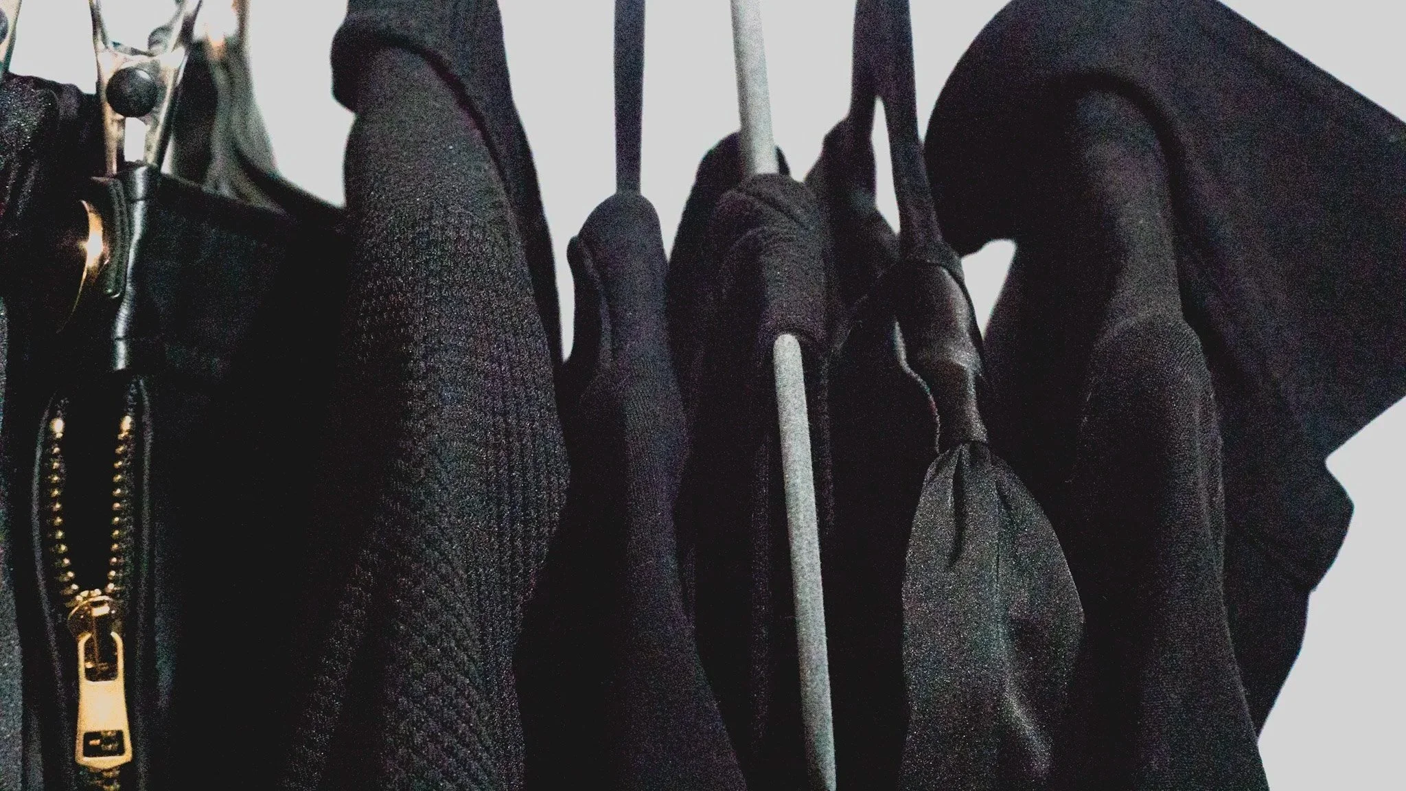 Close-up view of hanging black jackets and coats on a clothing rack, with textured fabrics and metal hangers visible.