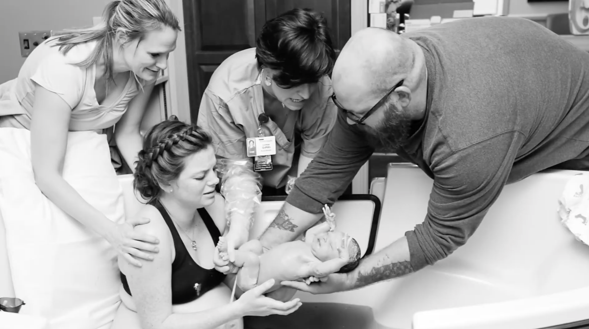 A woman giving birth in a hospital bed with her partner and medical staff assisting, all gathered around her during labor.