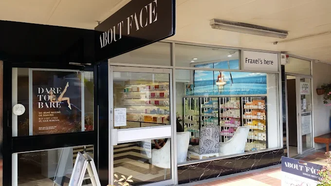 The exterior of a retail store named 'ABOUT FACE' with large glass windows displaying shelves of beauty products, and a sign that says 'Fraxel's here'.