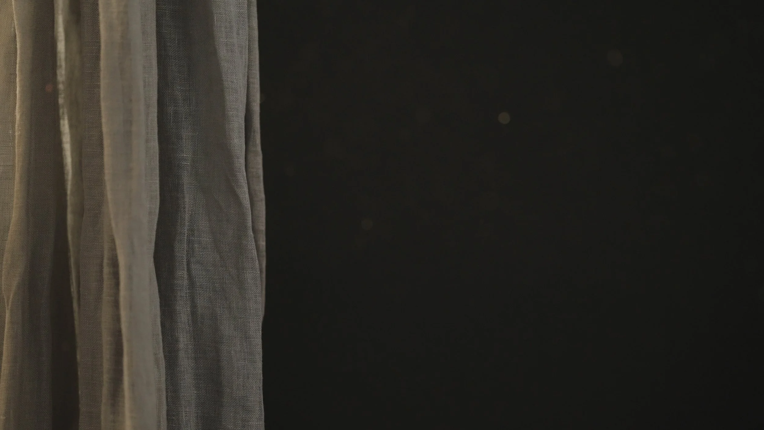Partial view of a sheer curtain hanging on the left, with a dark background on the right.