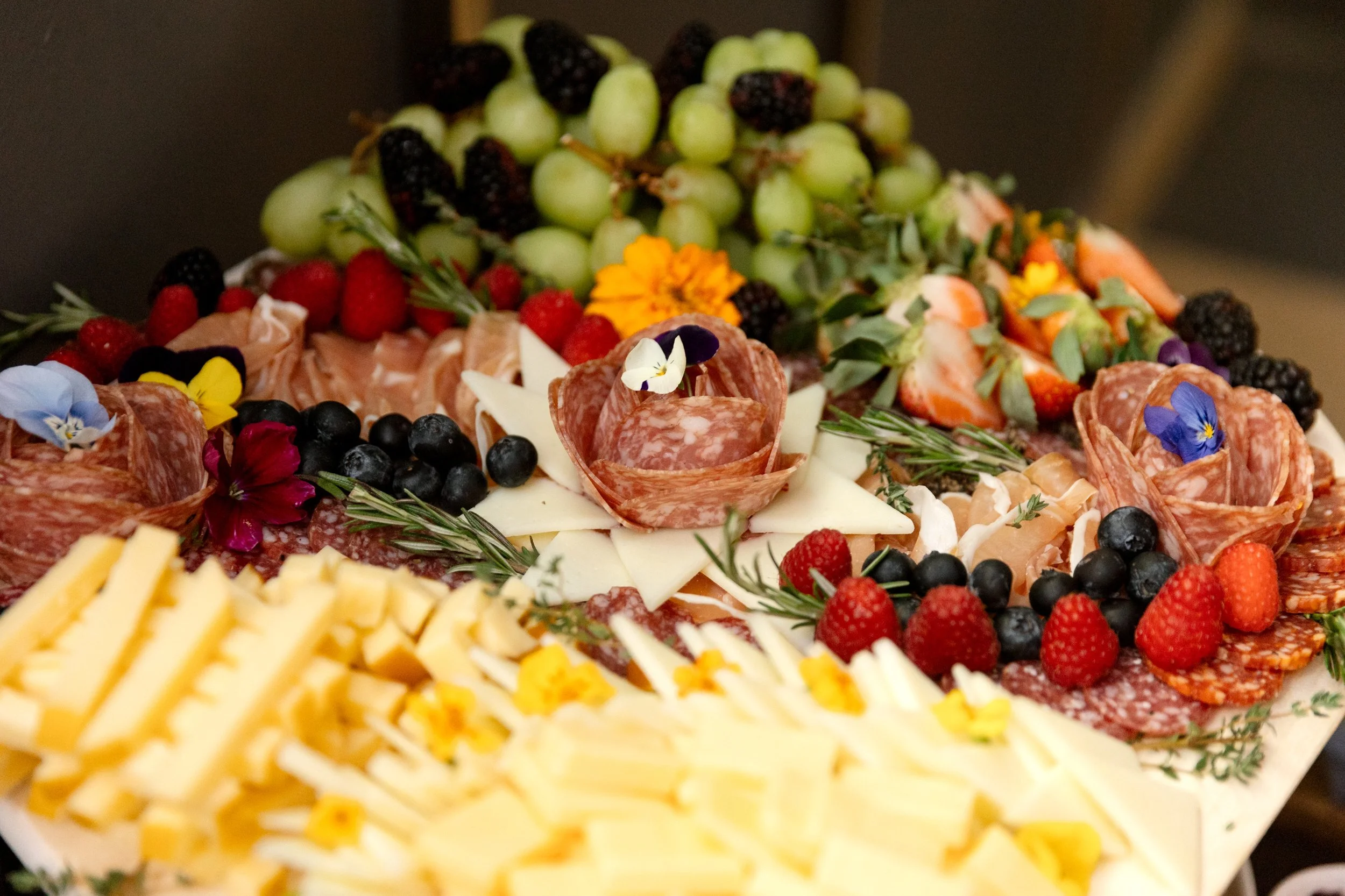 Cheese, cured meats, grapes, strawberries, blackberries, raspberries, blueberries, and edible flowers on a large platter.