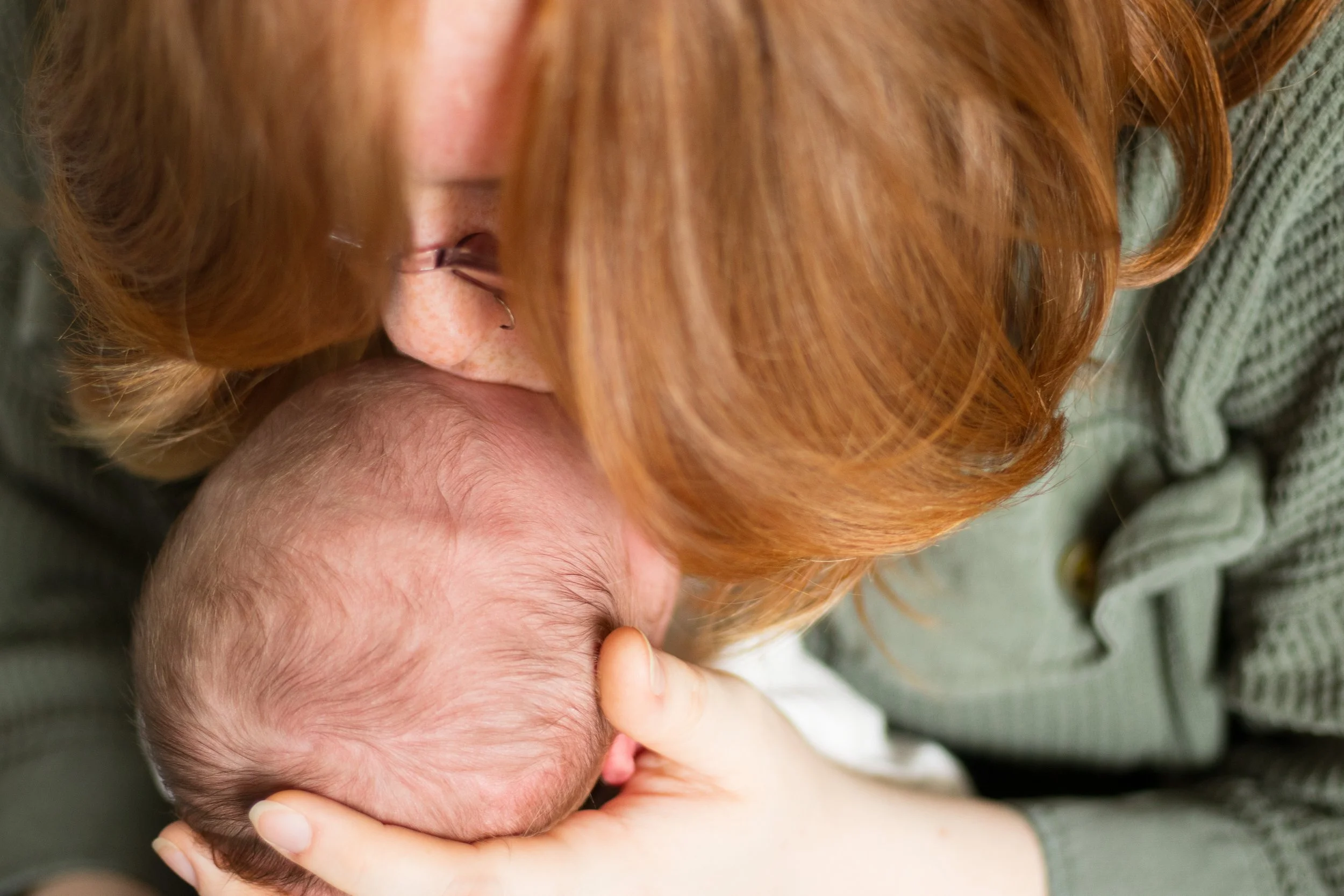 A woman with red hair gently breastfeeding a newborn baby.