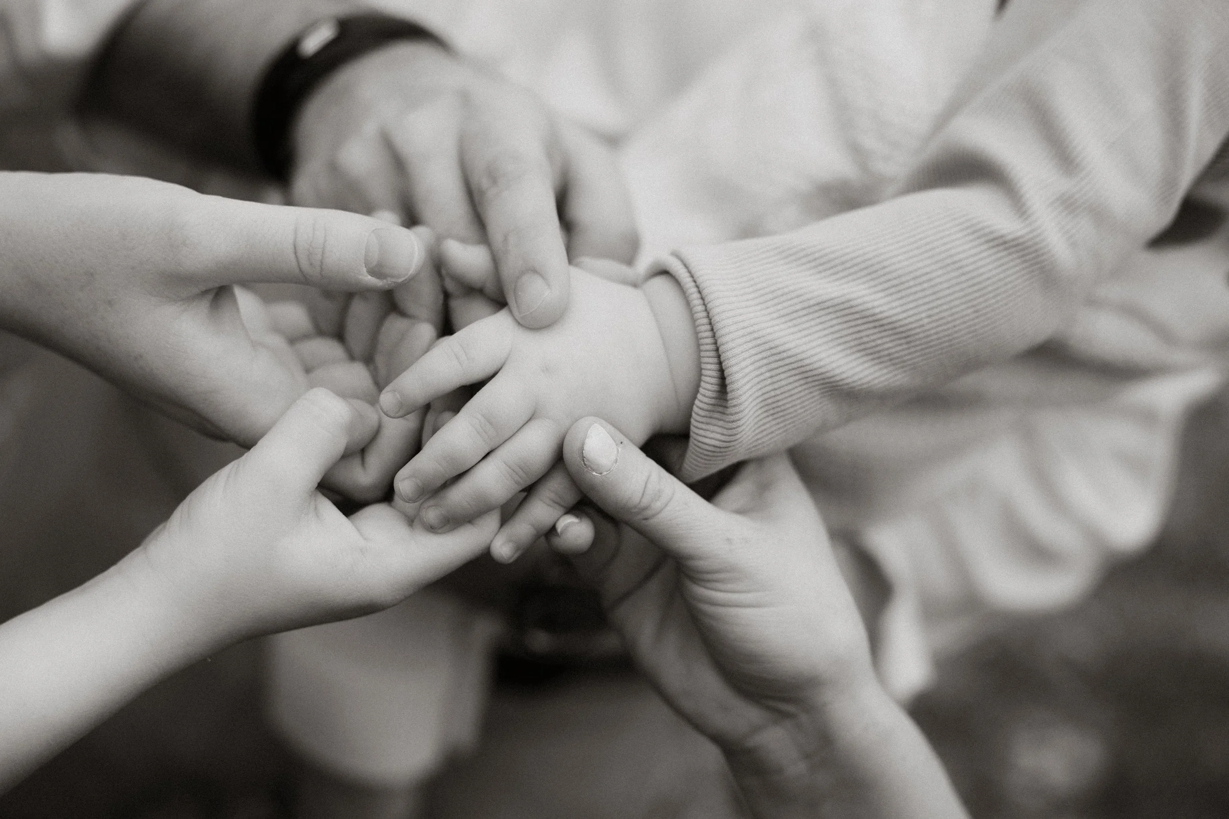 Multiple hands gently holding a child's hand, symbolizing care and support.