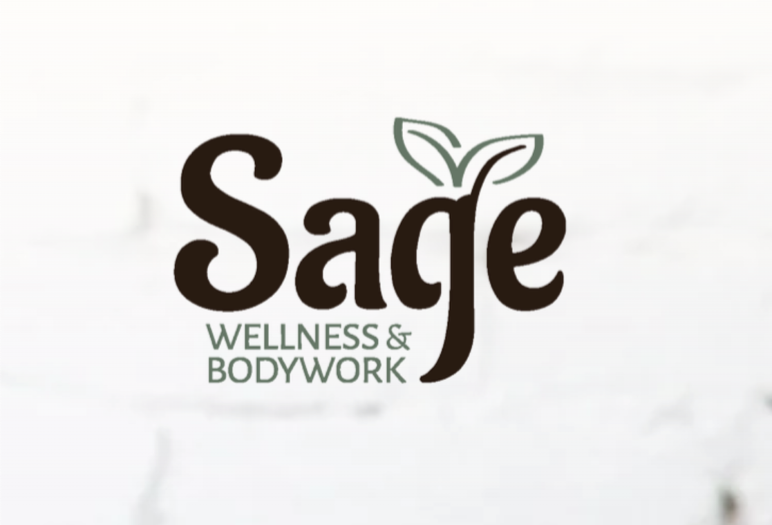 Close-up of a smiling woman with curly hair, wearing round glasses, hoop earrings, and a striped white top, indoors with some chairs and a window in the background.