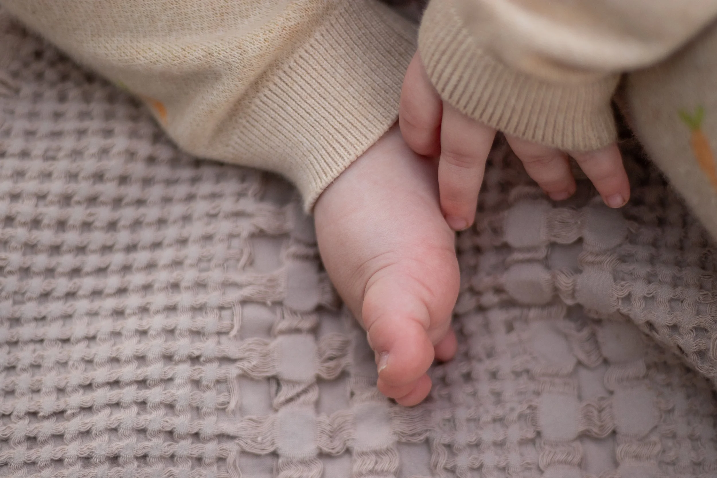 A close-up of two hands, one child's and one adult's, holding each other on a textured blanket.