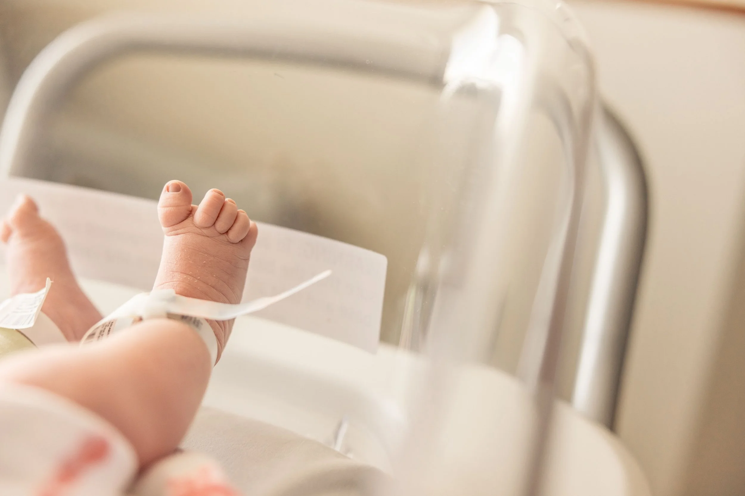 Close-up of a newborn baby’s tiny hand with a hospital wristband, lying in a hospital bassinet or crib.