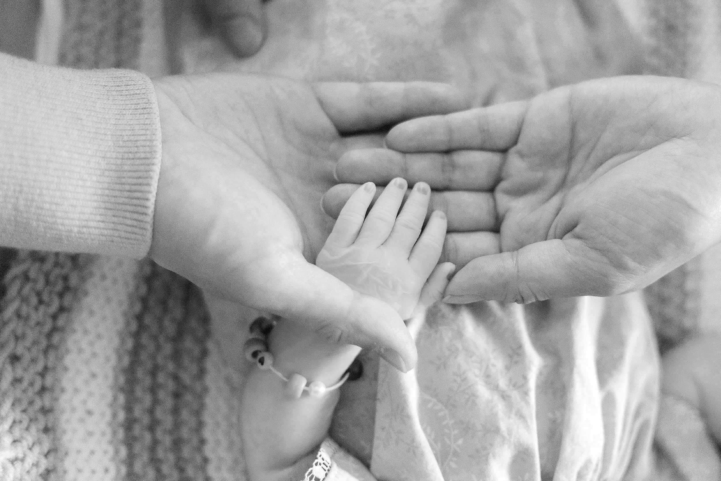 A close-up of two hands, one child's and one adult's, holding each other on a textured blanket.