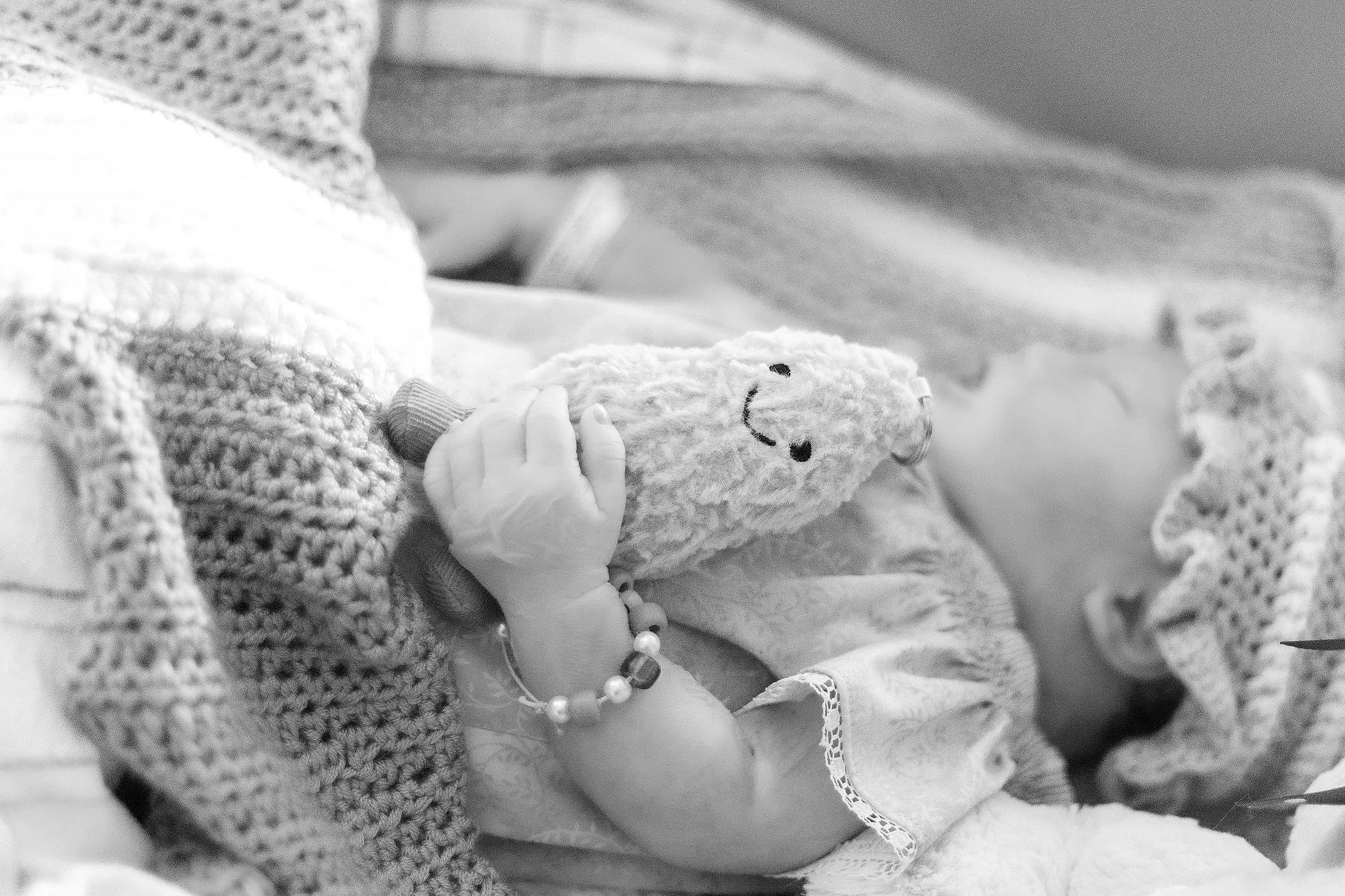 Close-up of a newborn baby’s tiny hand with a hospital wristband, lying in a hospital bassinet or crib.