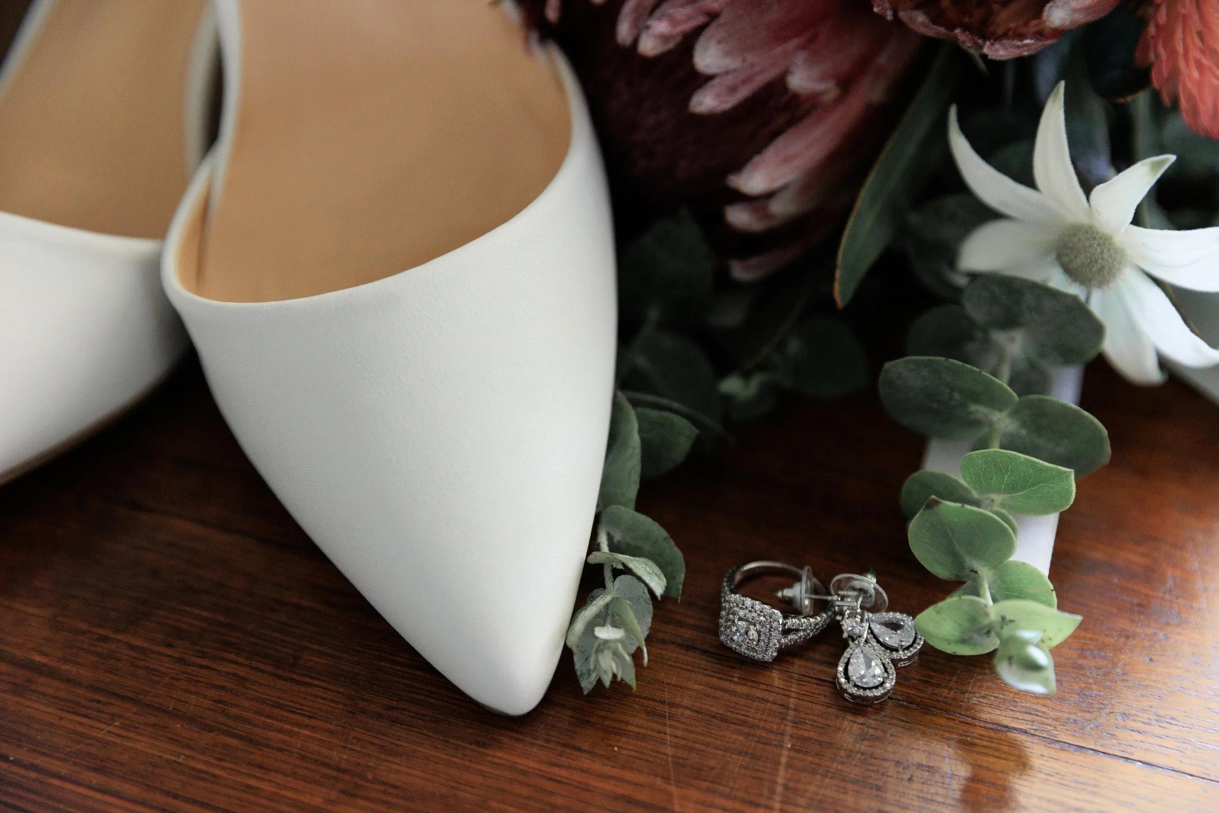 Two white ceramic cups, some jewelry, a white flower, and assorted greenery on a wooden surface.