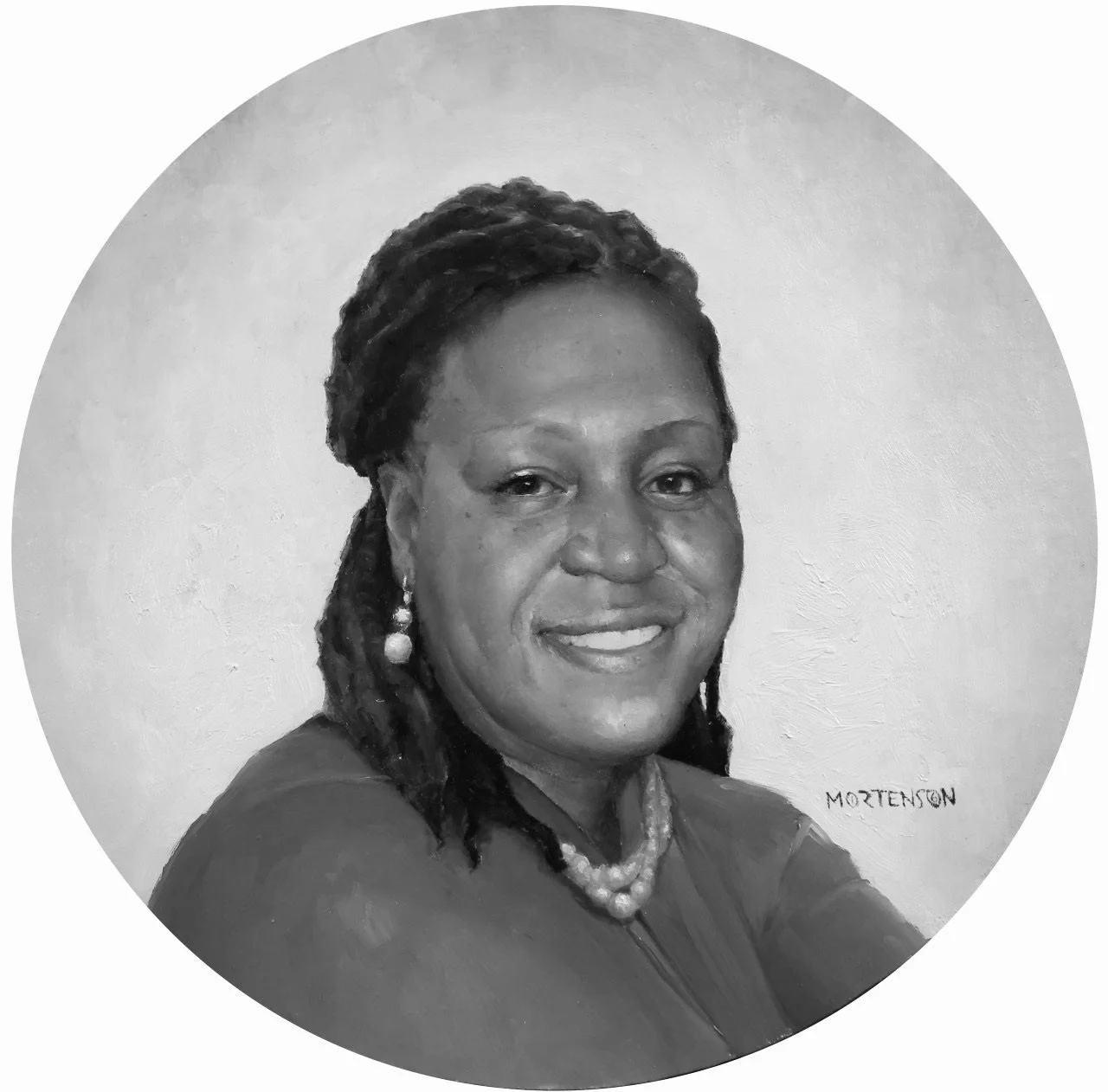 A woman with round glasses and earrings smiling in an indoor setting.