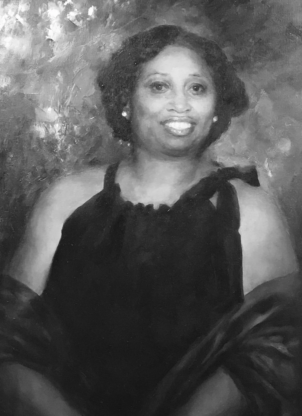 A close-up of a man with dark curly hair, clear round glasses, a beard, and a nose ring, sitting indoors with a neutral background and a green plant in the background.