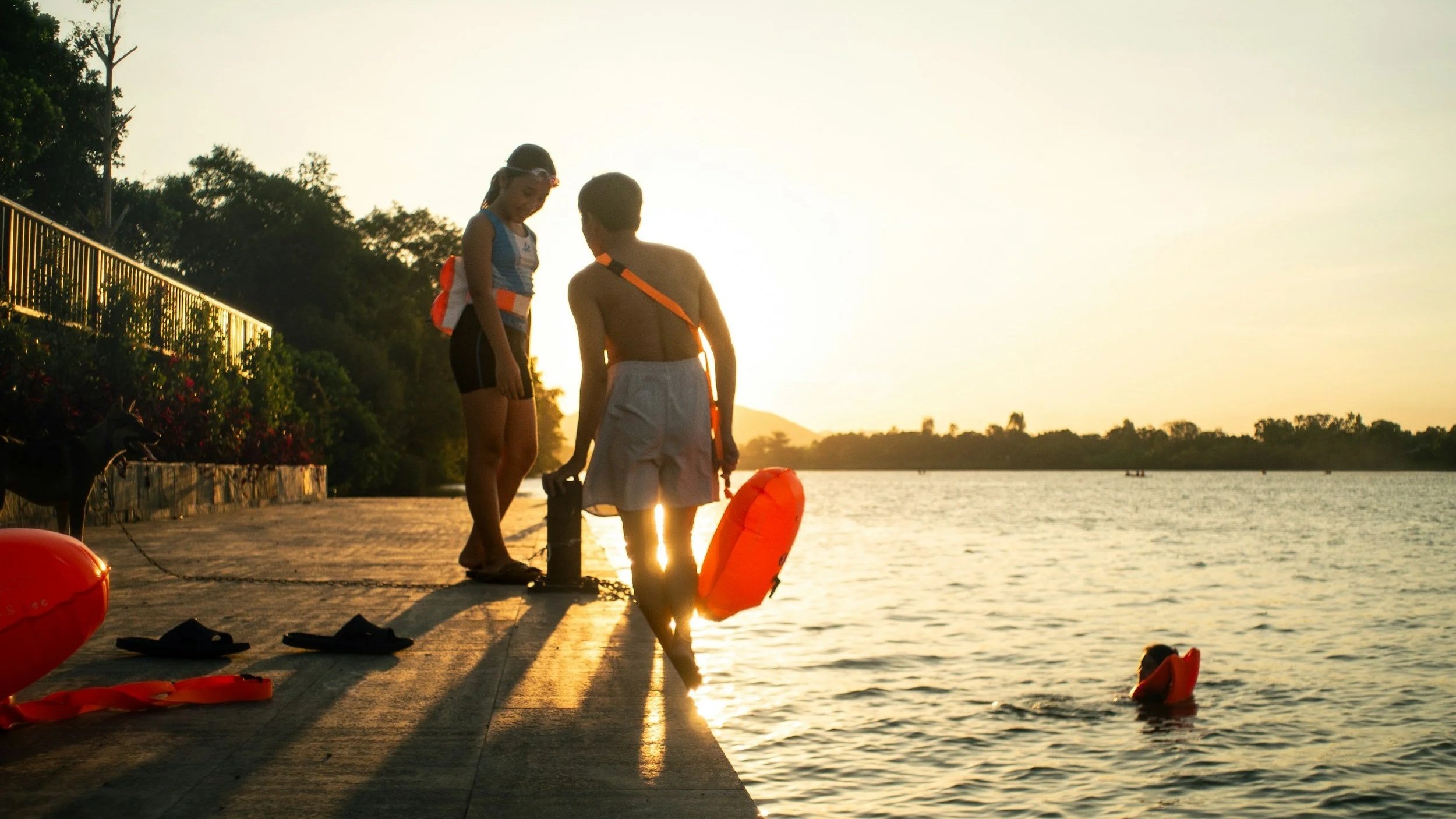 Two women wearing swim buoys near the edge of a river.