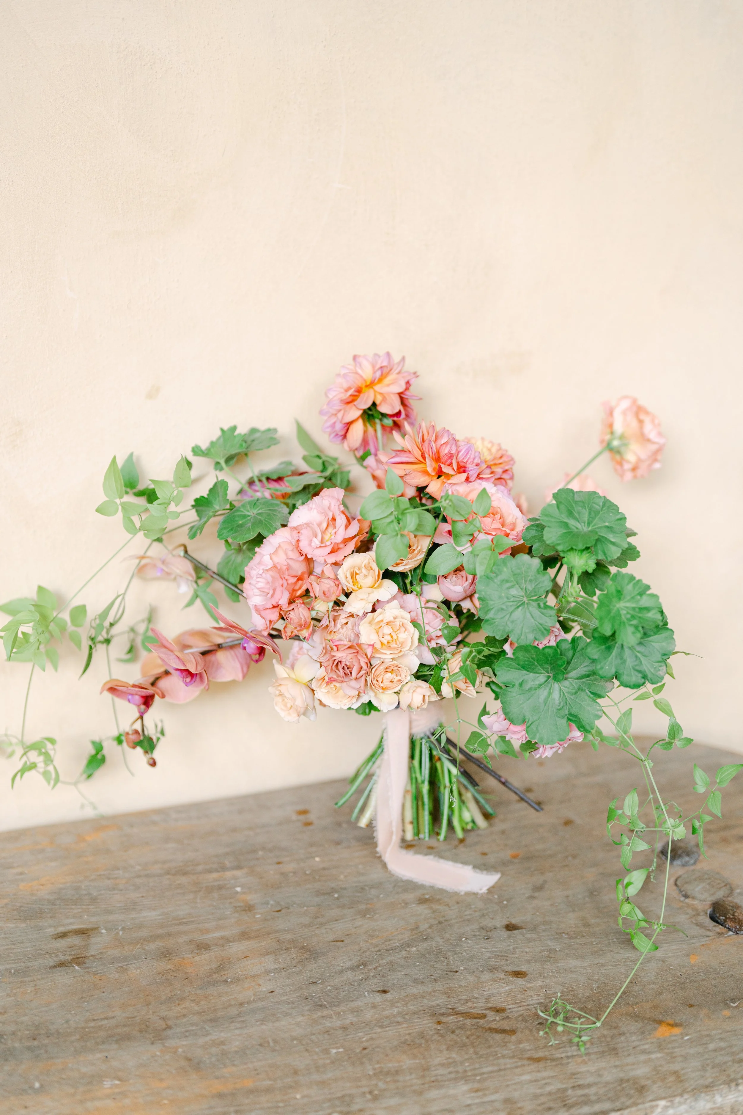 Ramo de flores en tonos rosados y verdes en una mesa de madera contra una pared beige