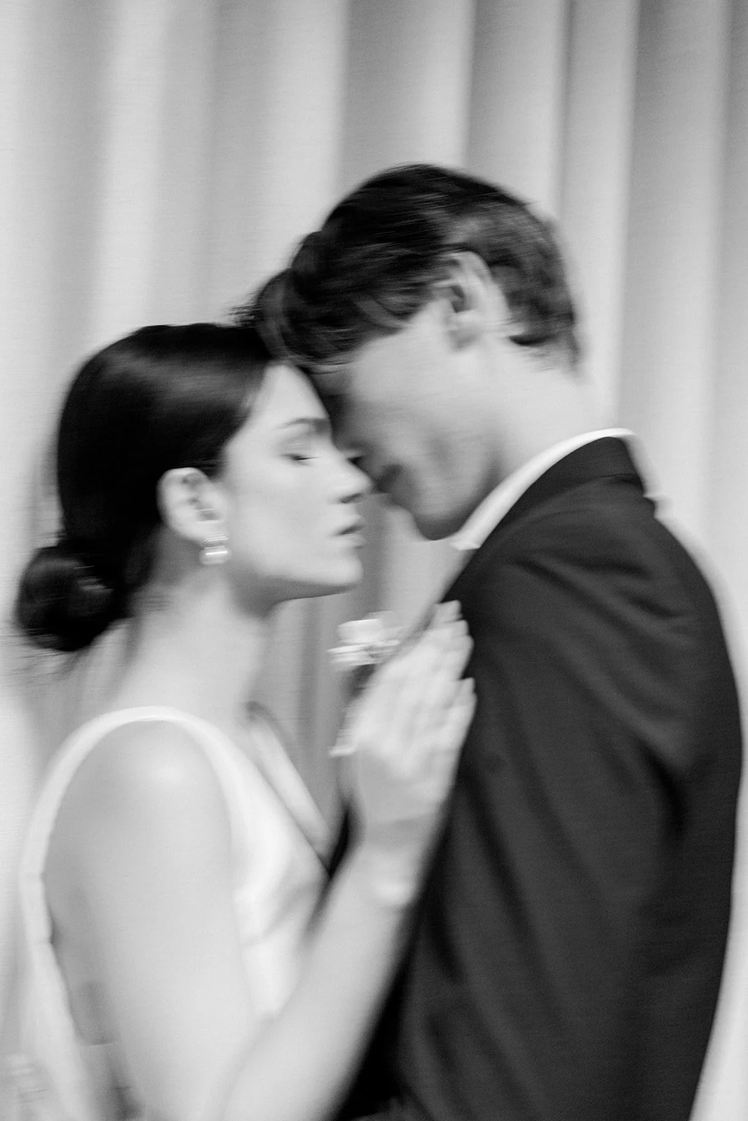 Pareja bailando, la mujer con vestido blanco y el hombre con traje oscuro, en un ambiente íntimo con cortinas de fondo.