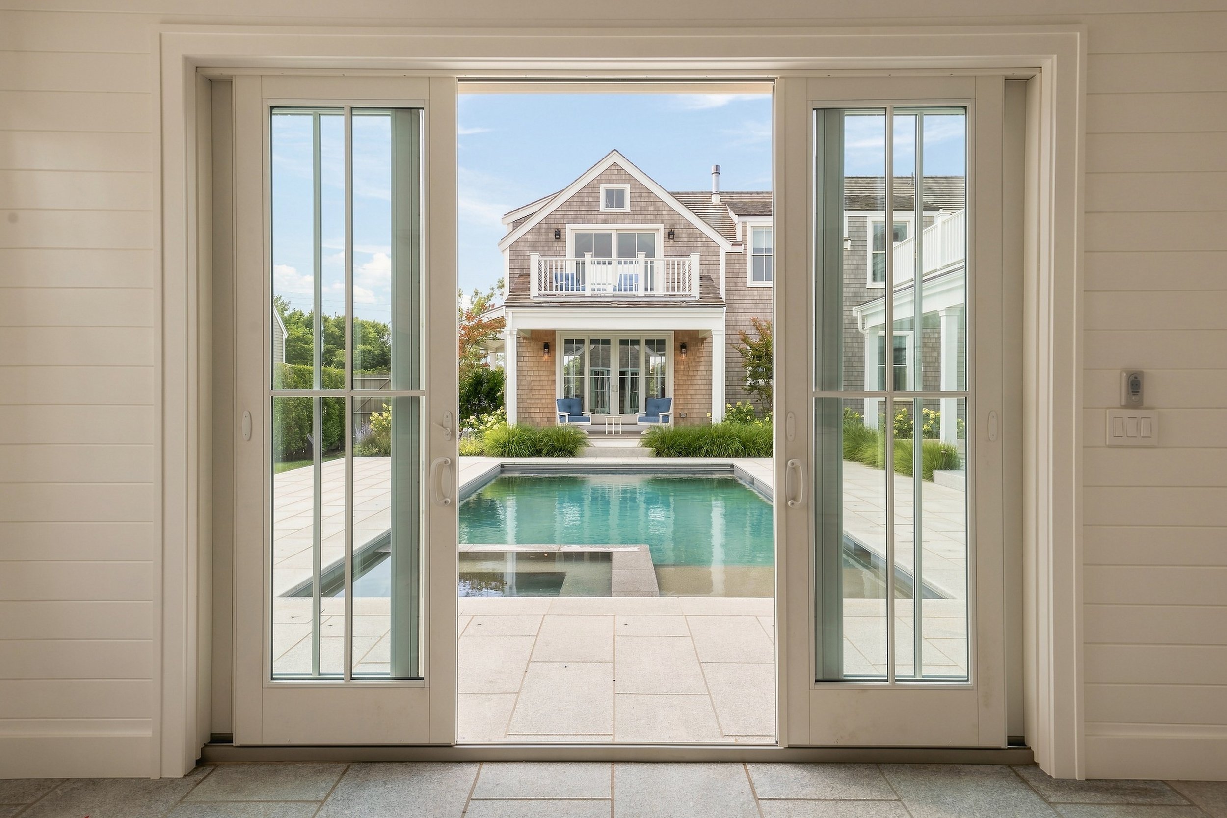 View through glass doors across the pool to a two-story cedar-shingle guest wing