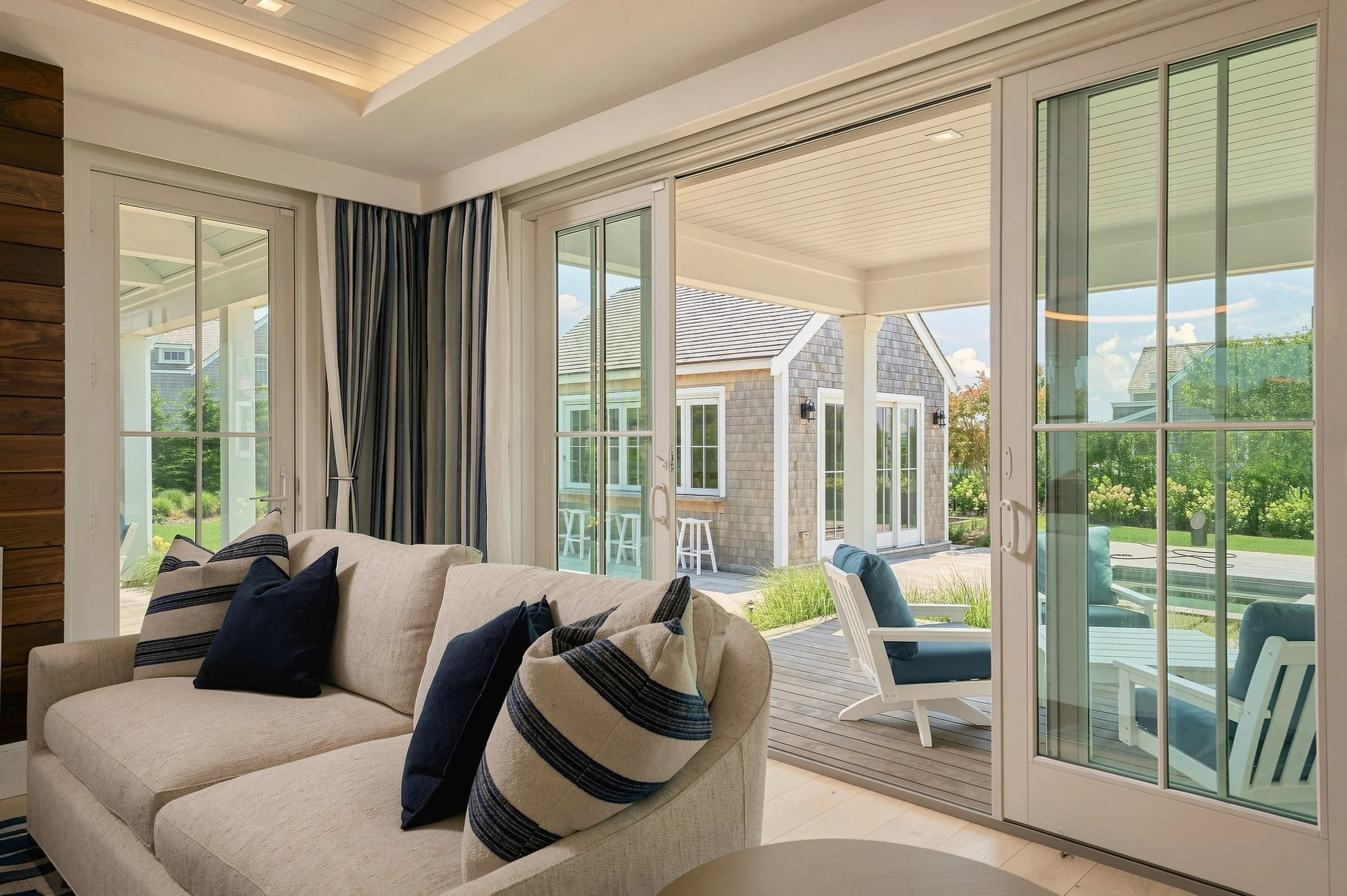 Coastal living room with white seating and folding glass doors opening to the pool terrace