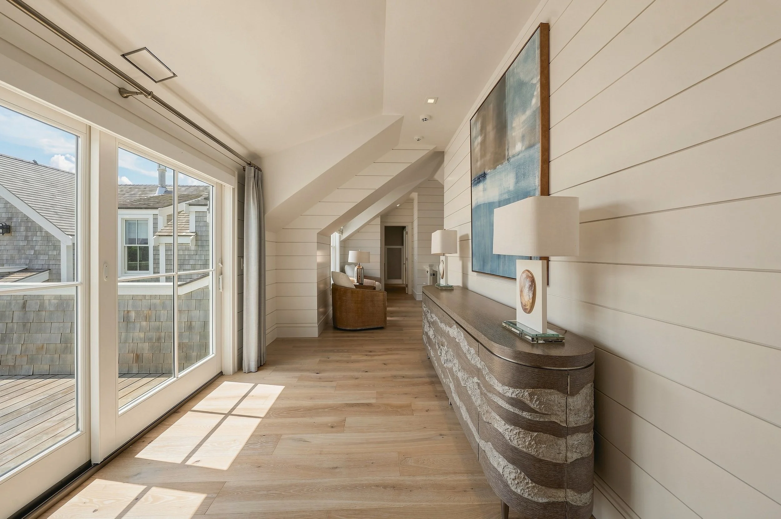Sunlit upper hallway with white shiplap walls, pale oak floors and doors opening to a roof deck