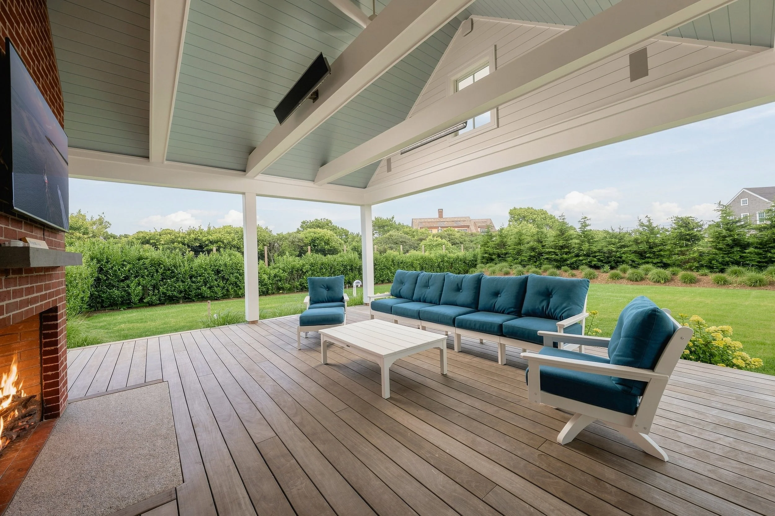 Covered outdoor lounge with blue seating, a vaulted ceiling, television and brick fireplace