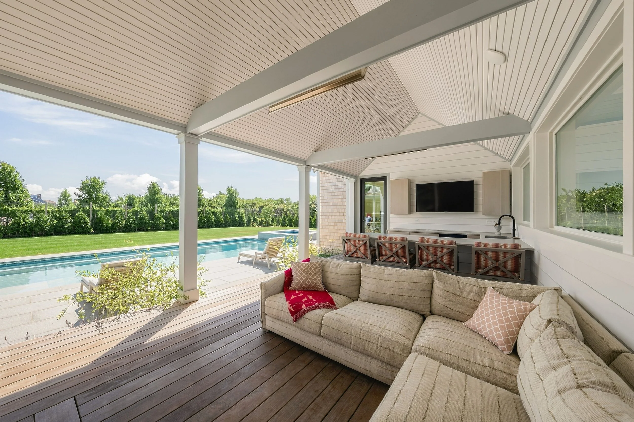 Covered outdoor living area with sectional seating, a television and poolside bar at the Sconset home