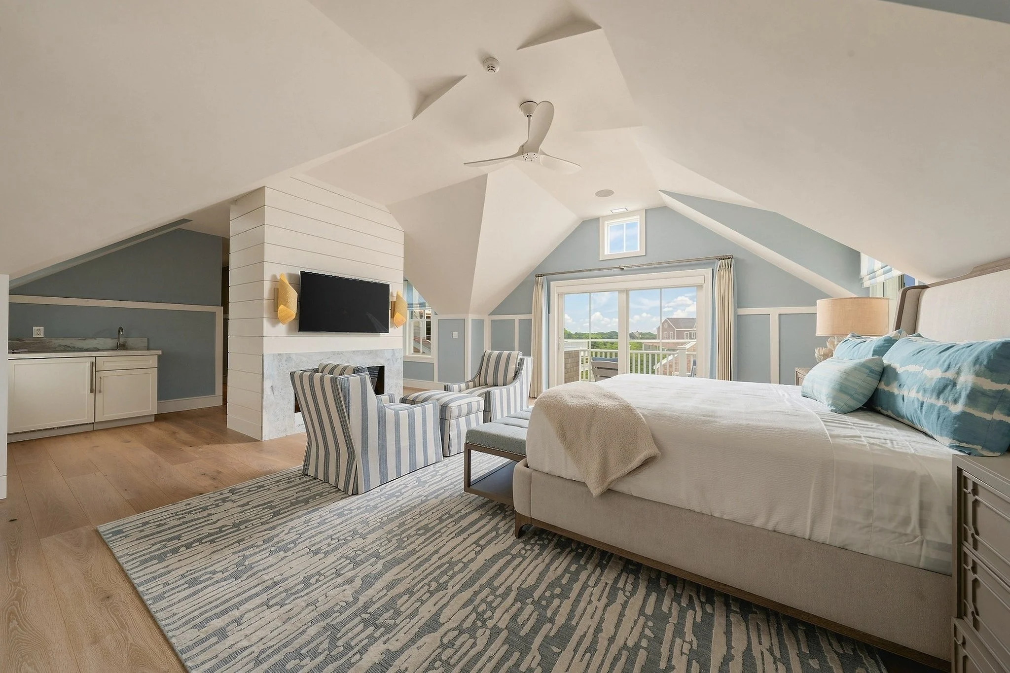 Vaulted blue-and-white bedroom with a fireplace, wet bar, balcony and exposed ceiling beams