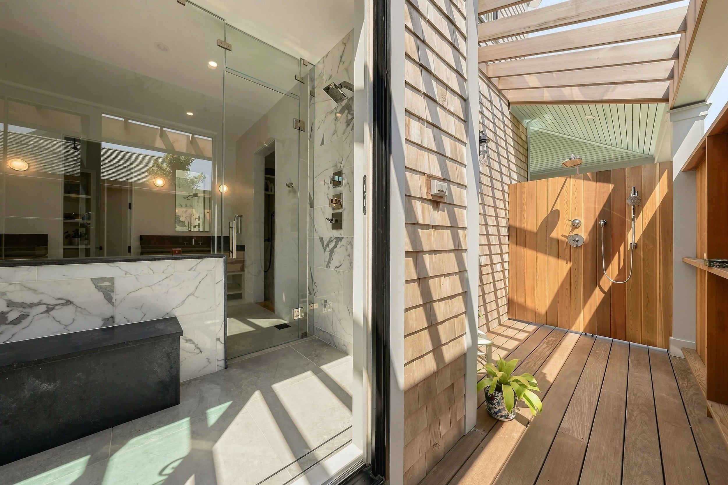 Indoor marble shower beside a cedar-lined outdoor shower beneath an open pergola