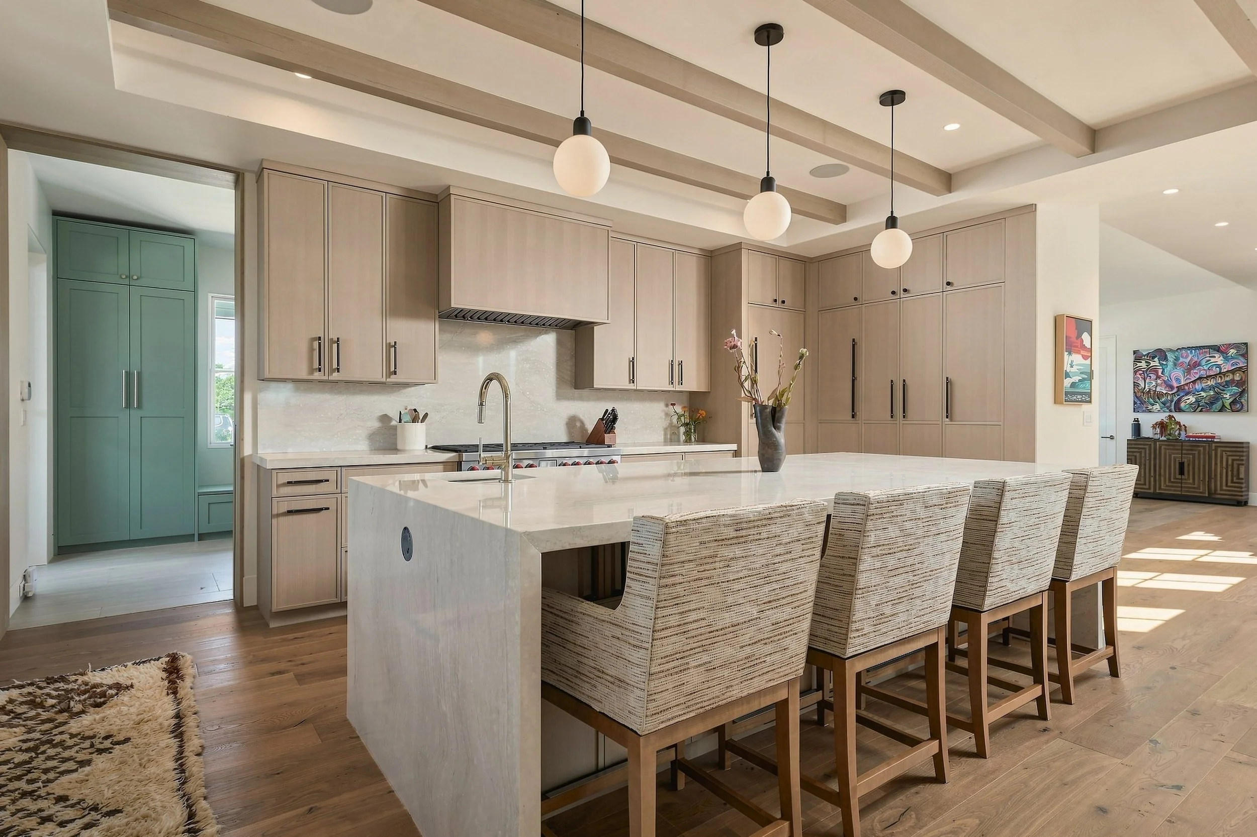 Modern kitchen with a waterfall island, five upholstered counter stools and light wood cabinetry
