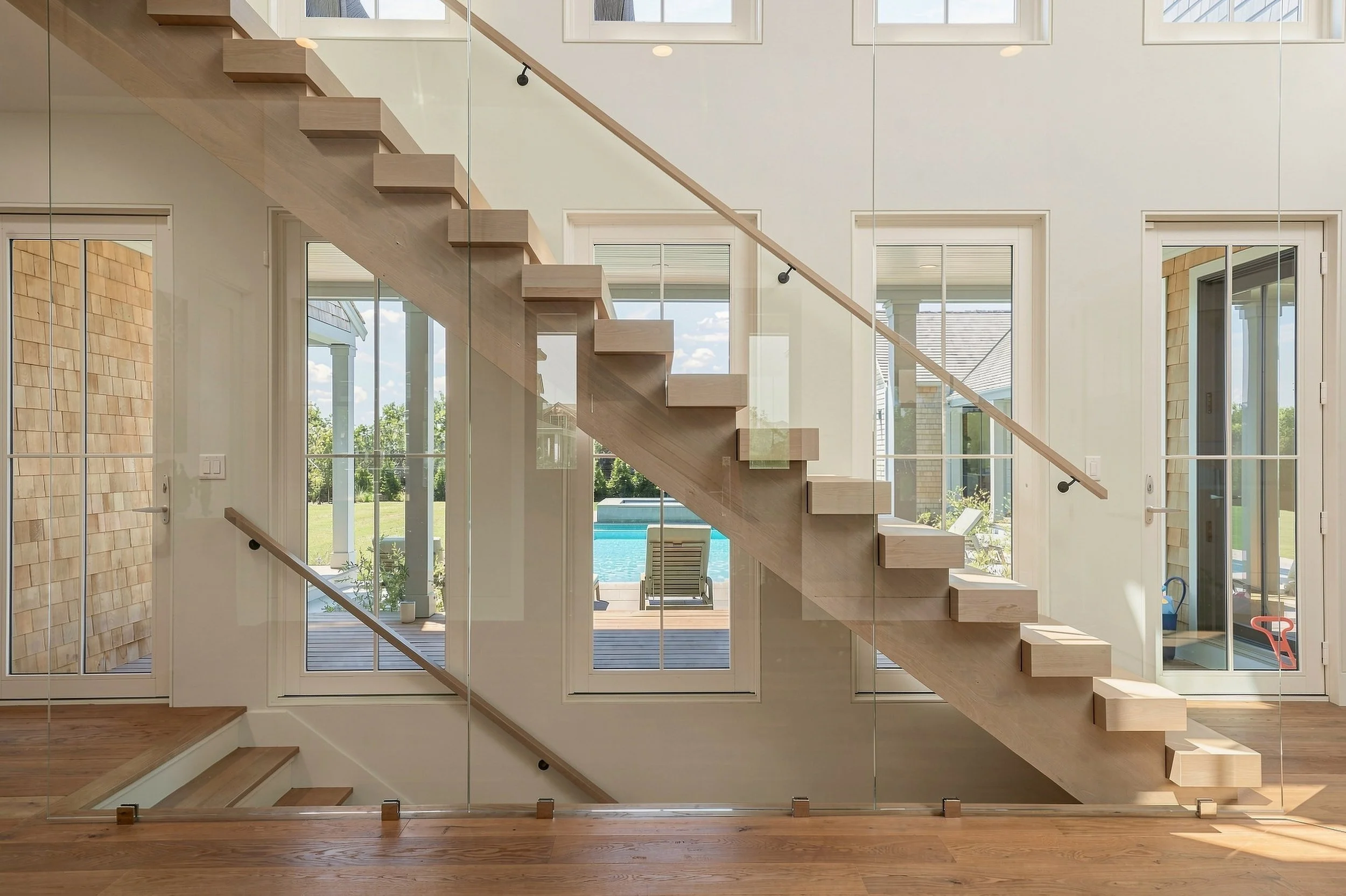 Side profile of the floating oak staircase with glass railings and views of the backyard pool