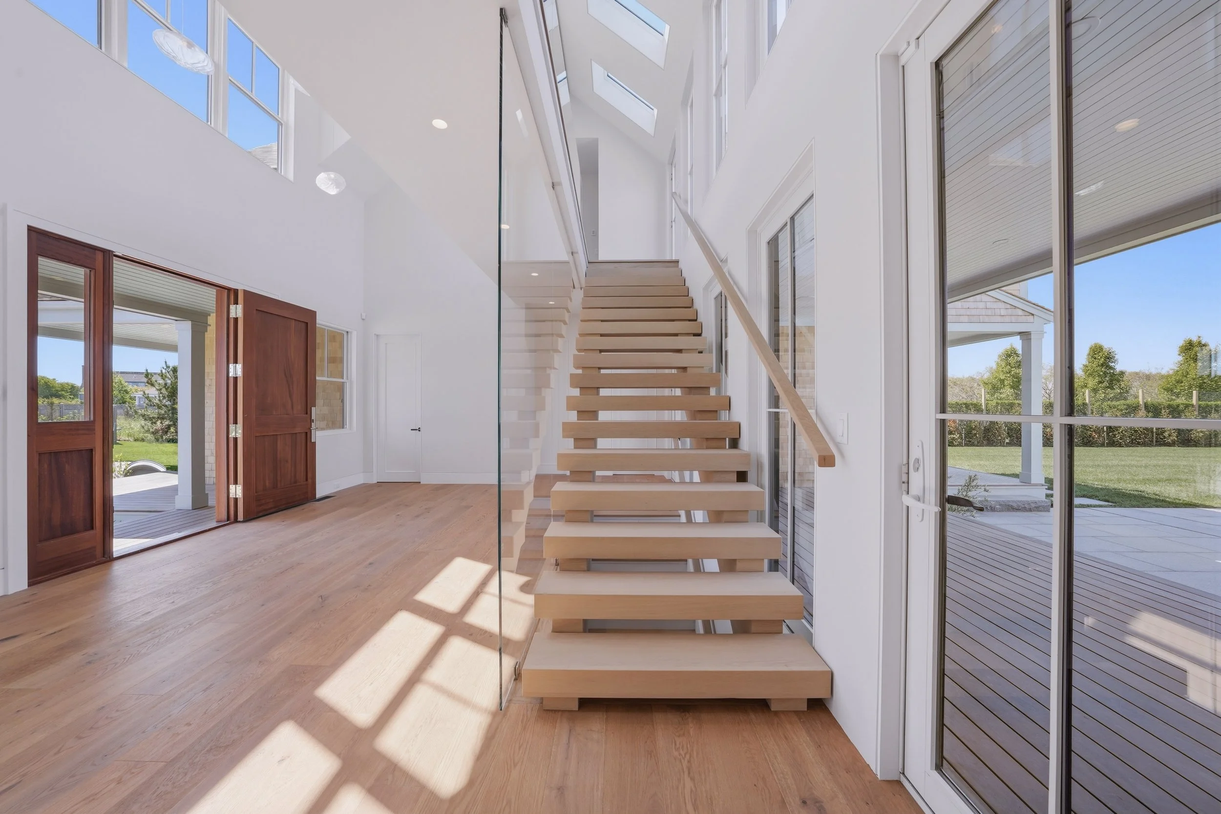 Light-filled entry hall with a floating oak staircase, glass railing, skylights and doors opening to the pool