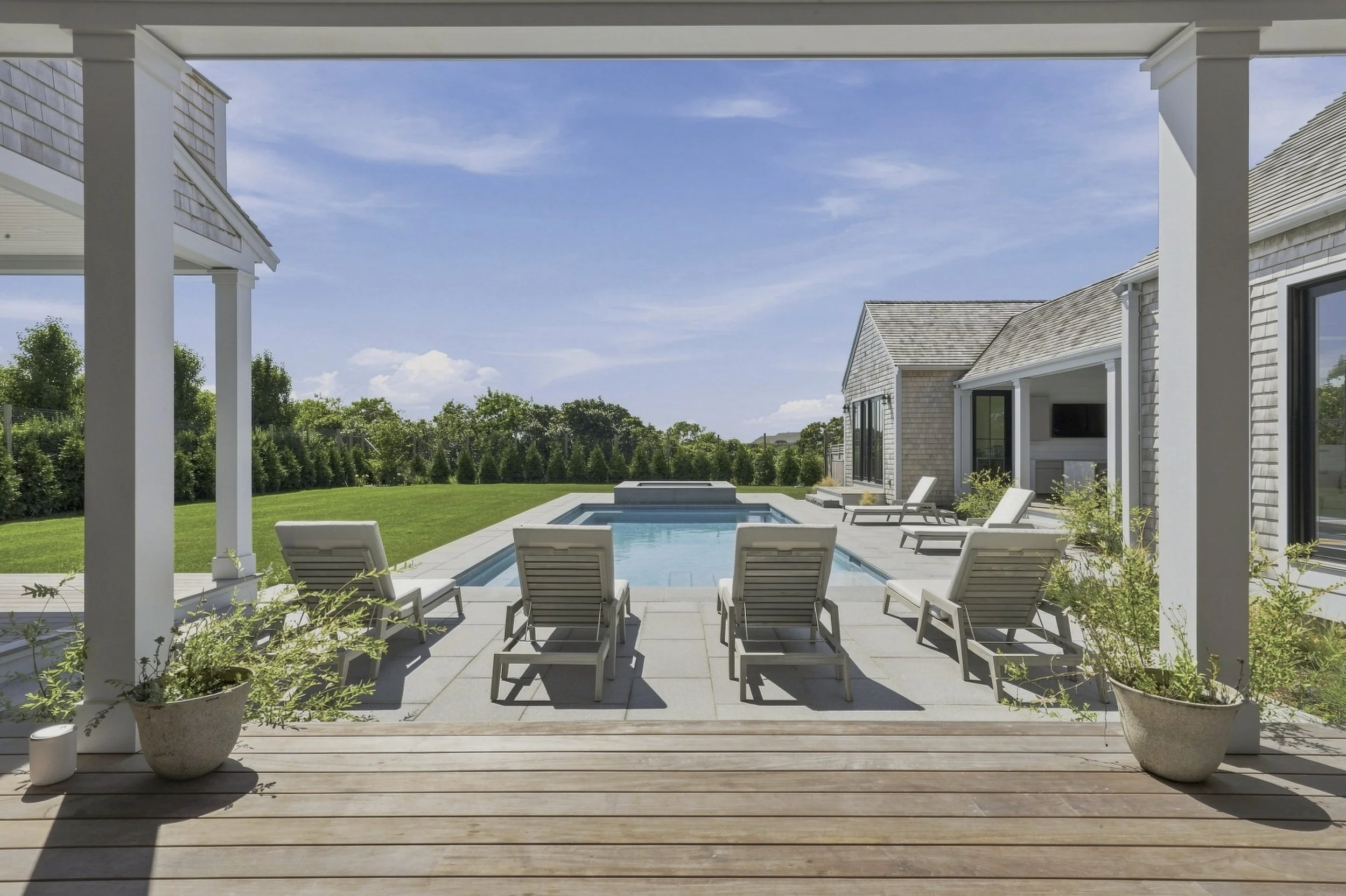 View from the covered porch across lounge chairs to the swimming pool, spa and landscaped lawn