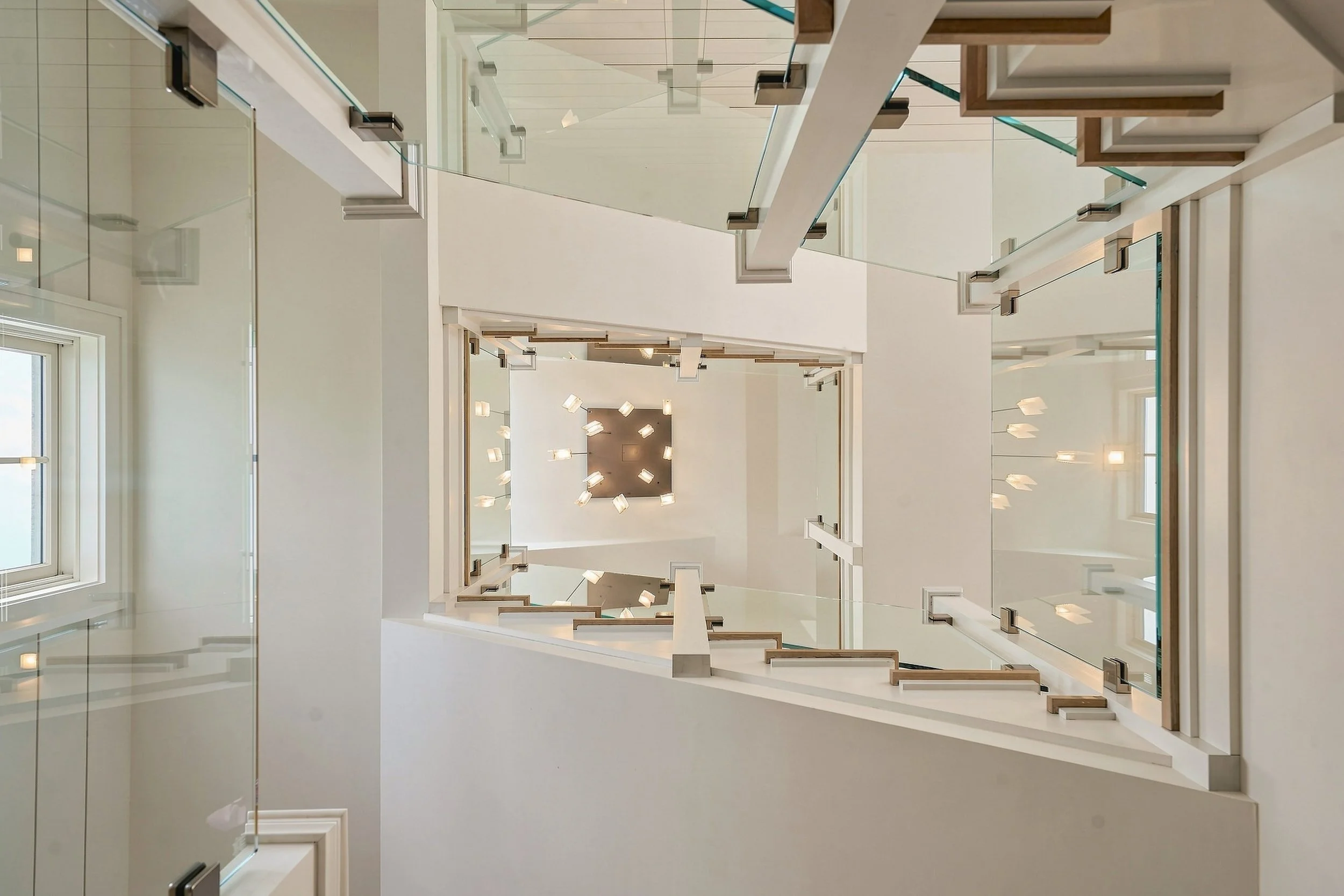 View down the open stairwell with glass railings, oak treads and a geometric pendant light
