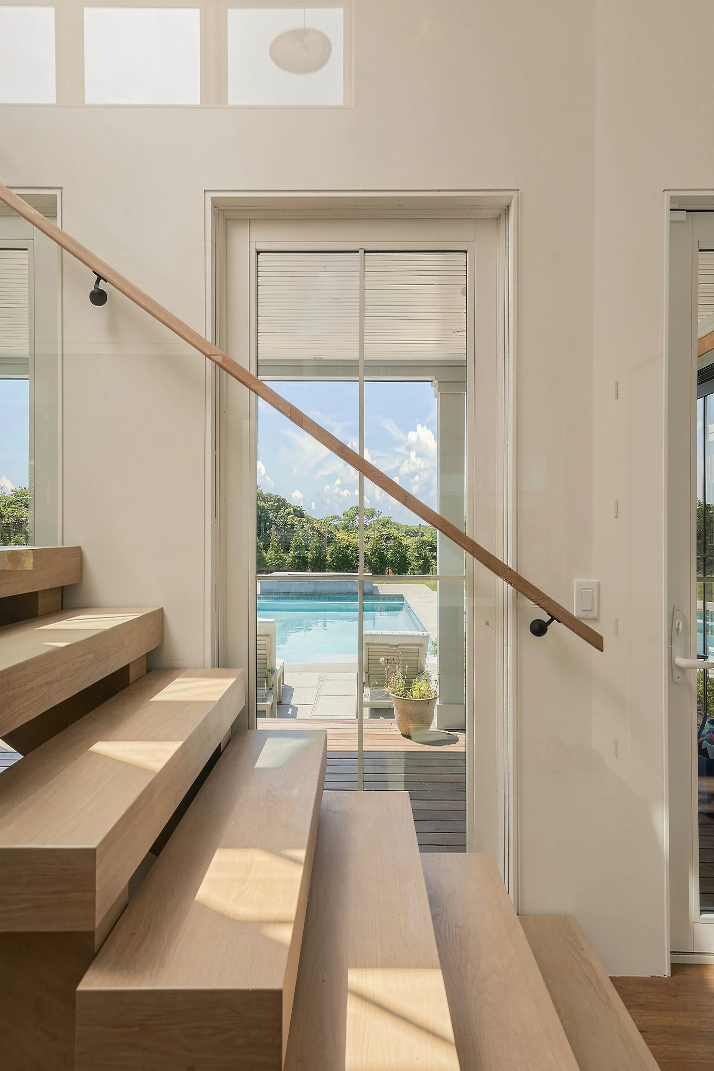 Close view of the floating oak staircase and glass railing with the backyard pool beyond
